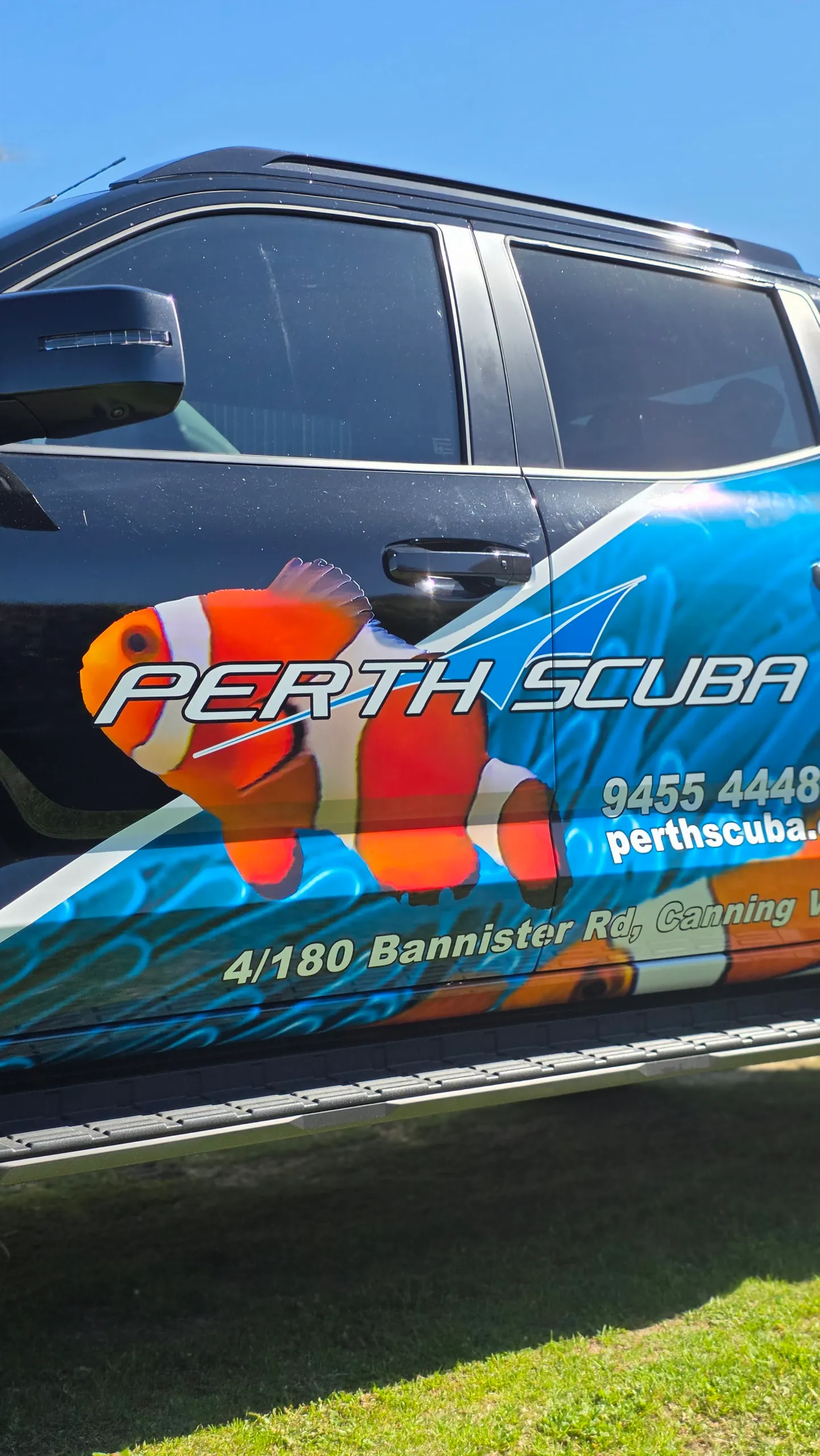 Perth Scuba clownfish and blue water graphics across the black Mitsubishi Triton doors