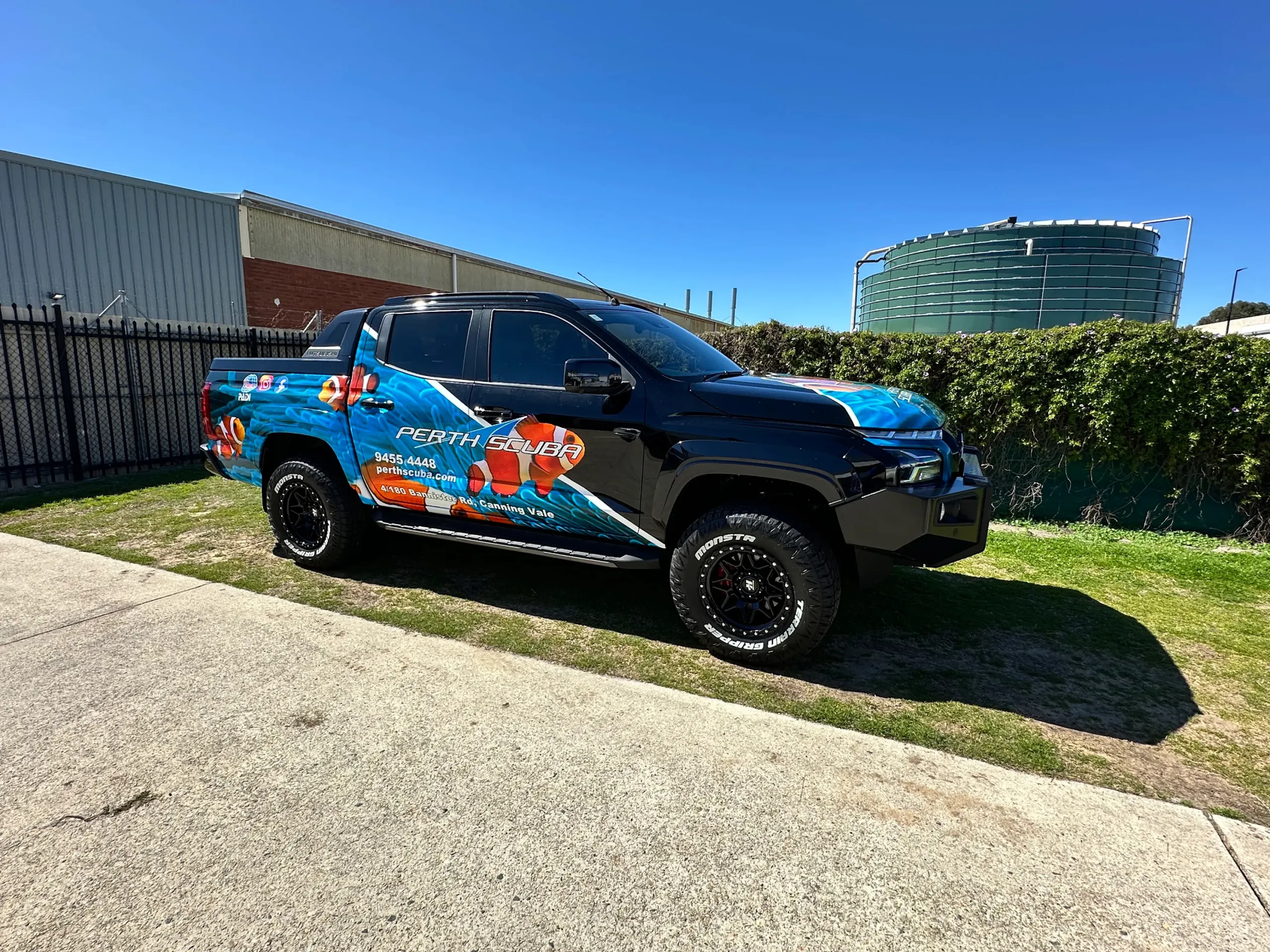 Black Mitsubishi Triton with blue Perth Scuba clownfish graphics parked on grass
