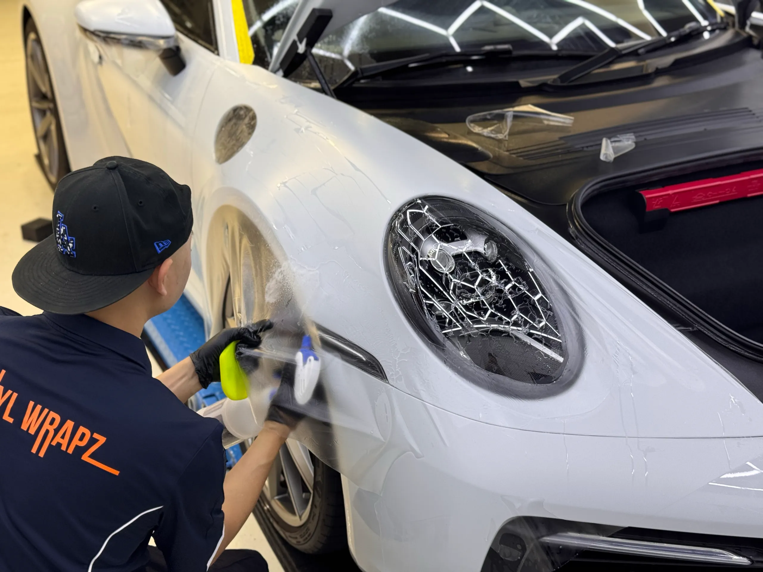 Installer fitting clear film around the white Porsche 911 front guard and headlight