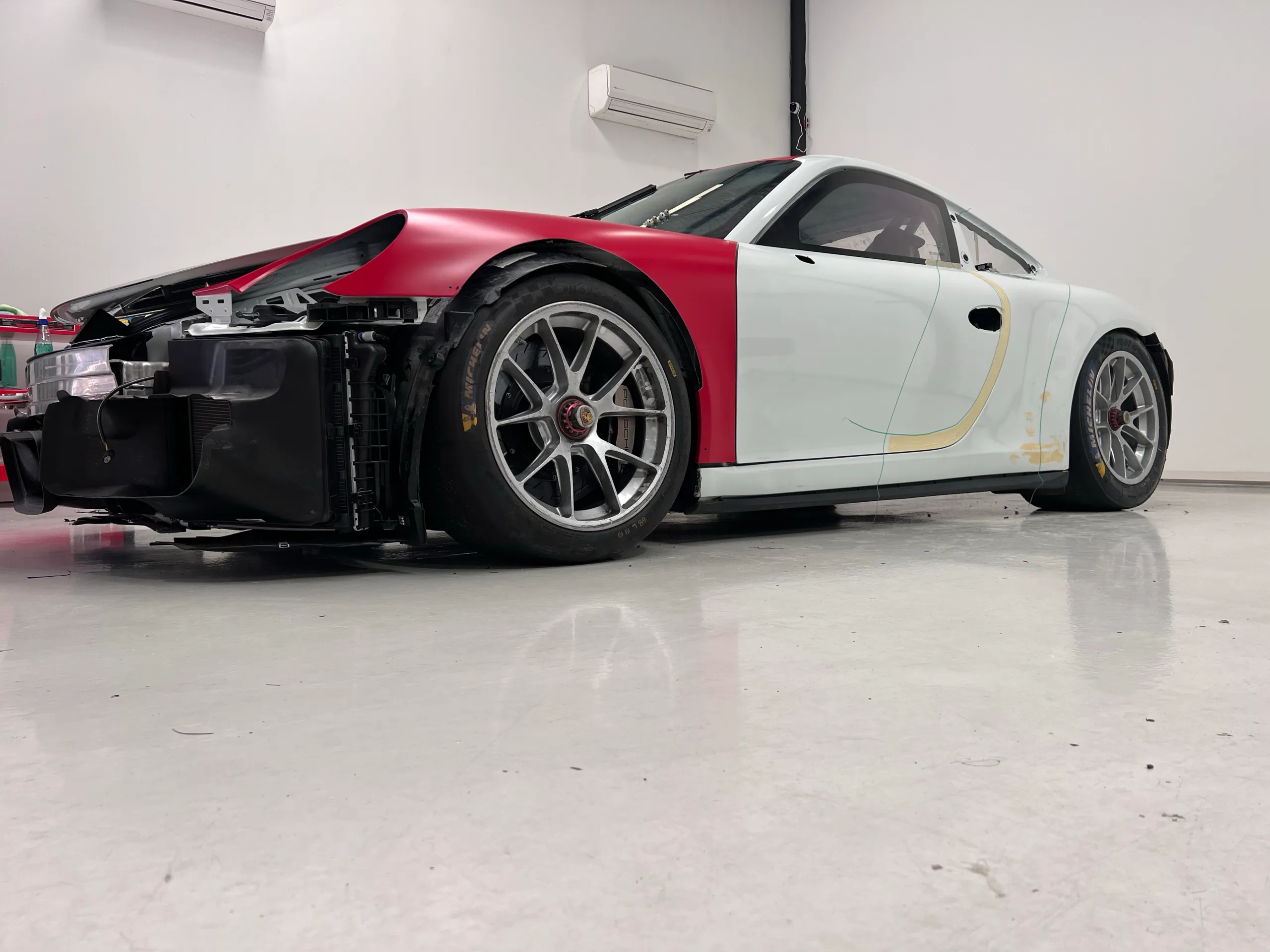 Porsche 911 race car during livery installation with red guards and its front bumper removed