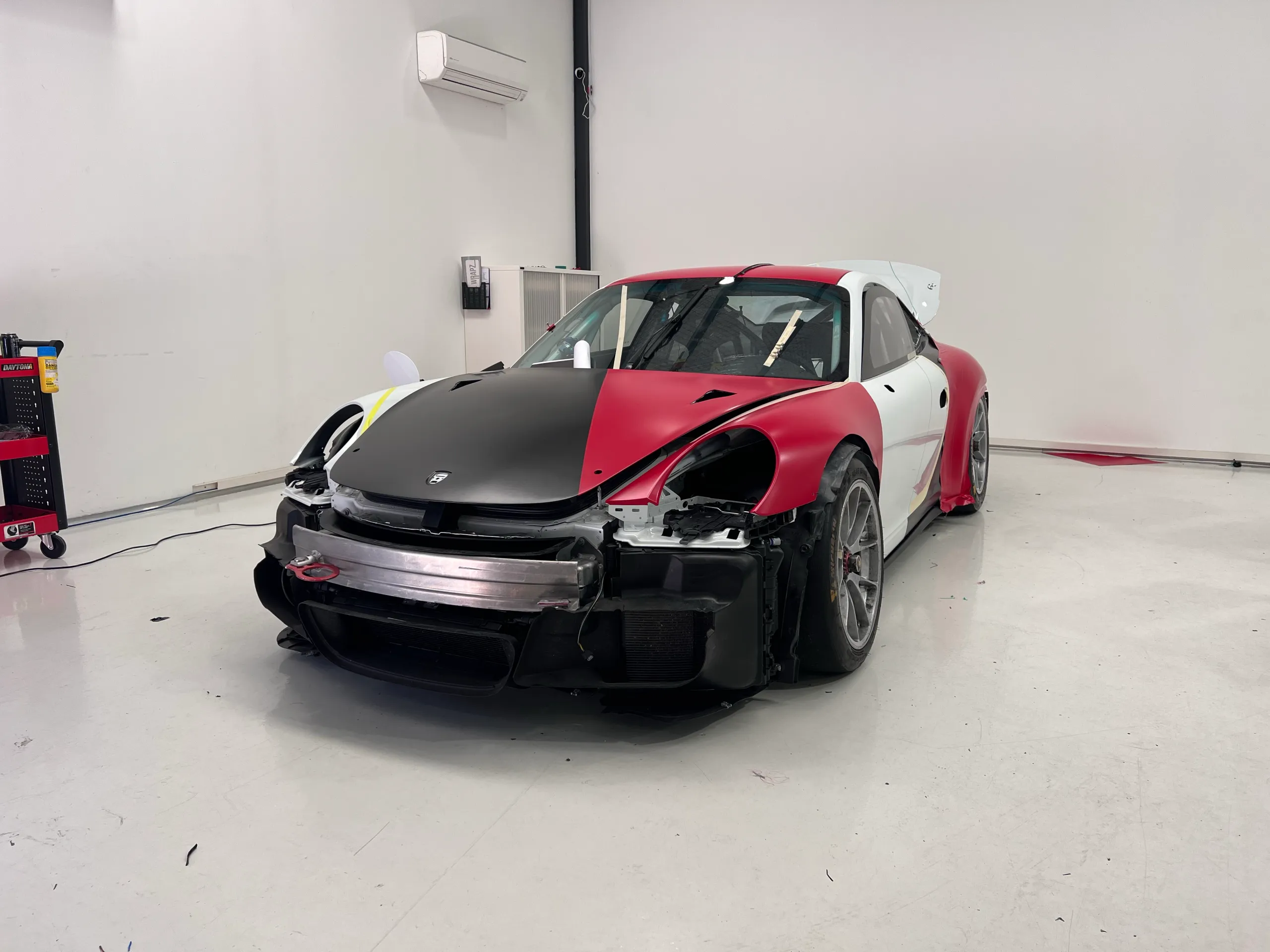 Red and black panels on a Porsche 911 during wrapping with front bumper and headlights removed