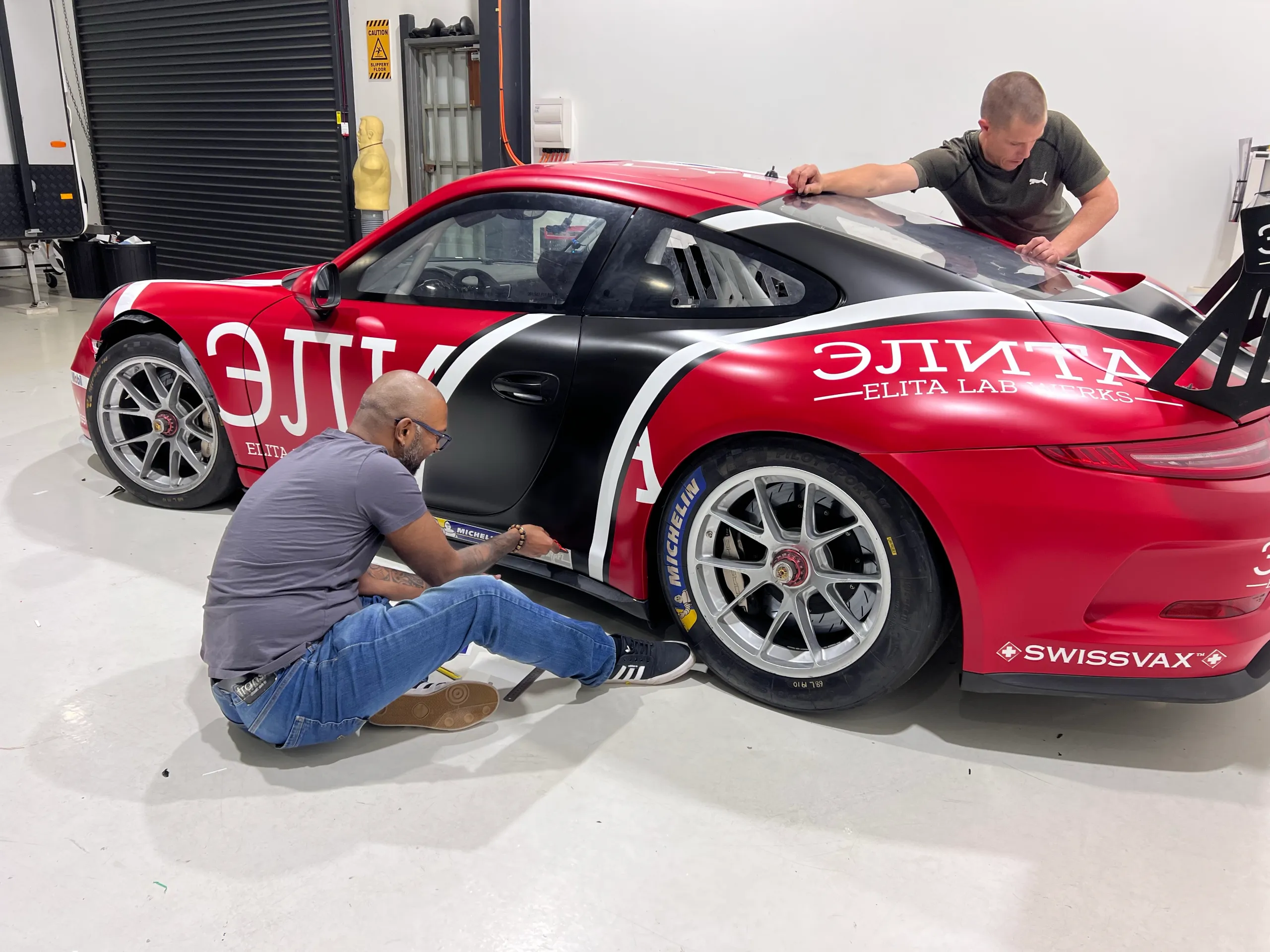 Installers fitting red, black and white Elita Lab Werks graphics to the Porsche 911 race car