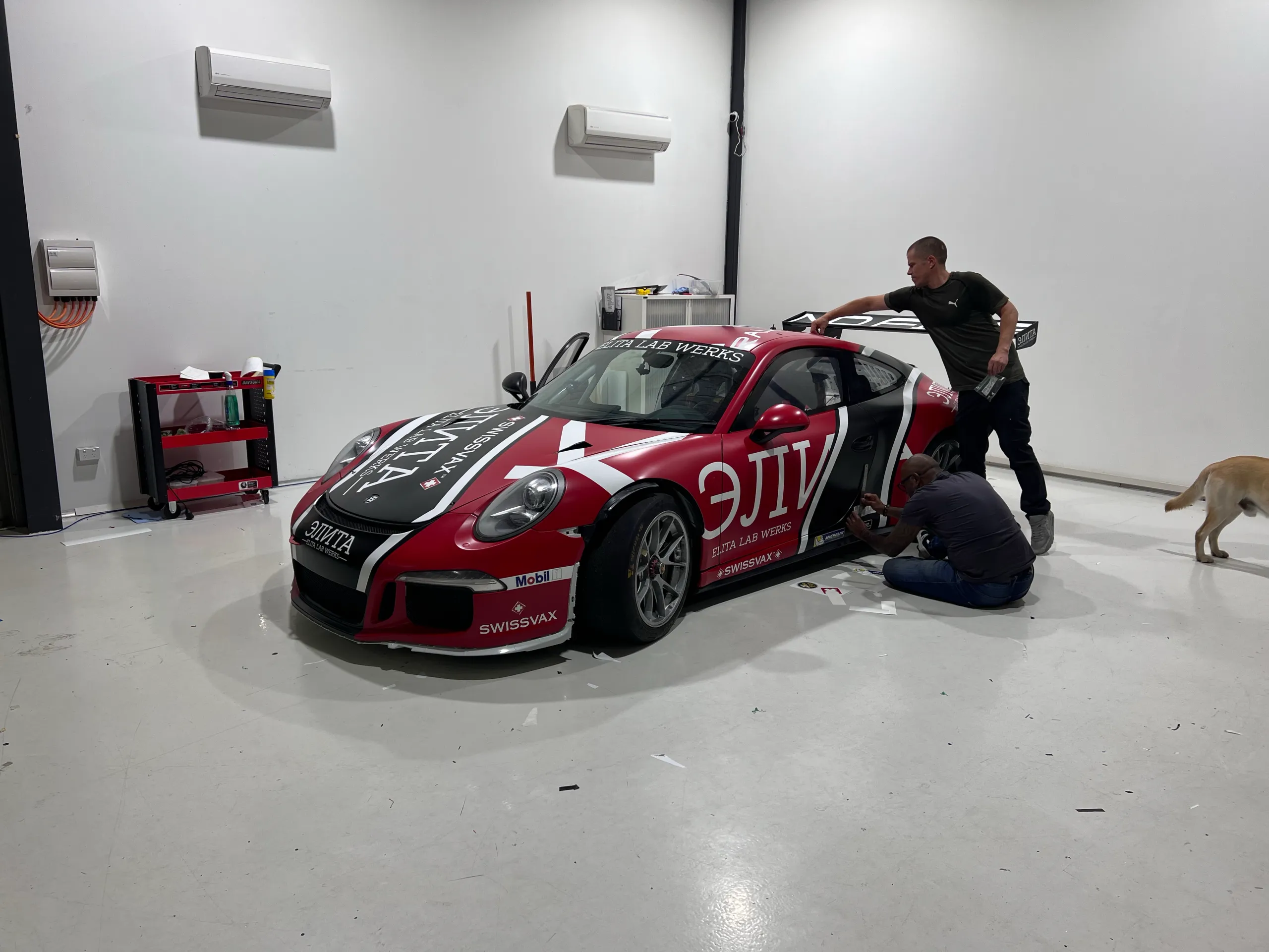 Installers finishing the Porsche 911 race livery with a dog beside the car