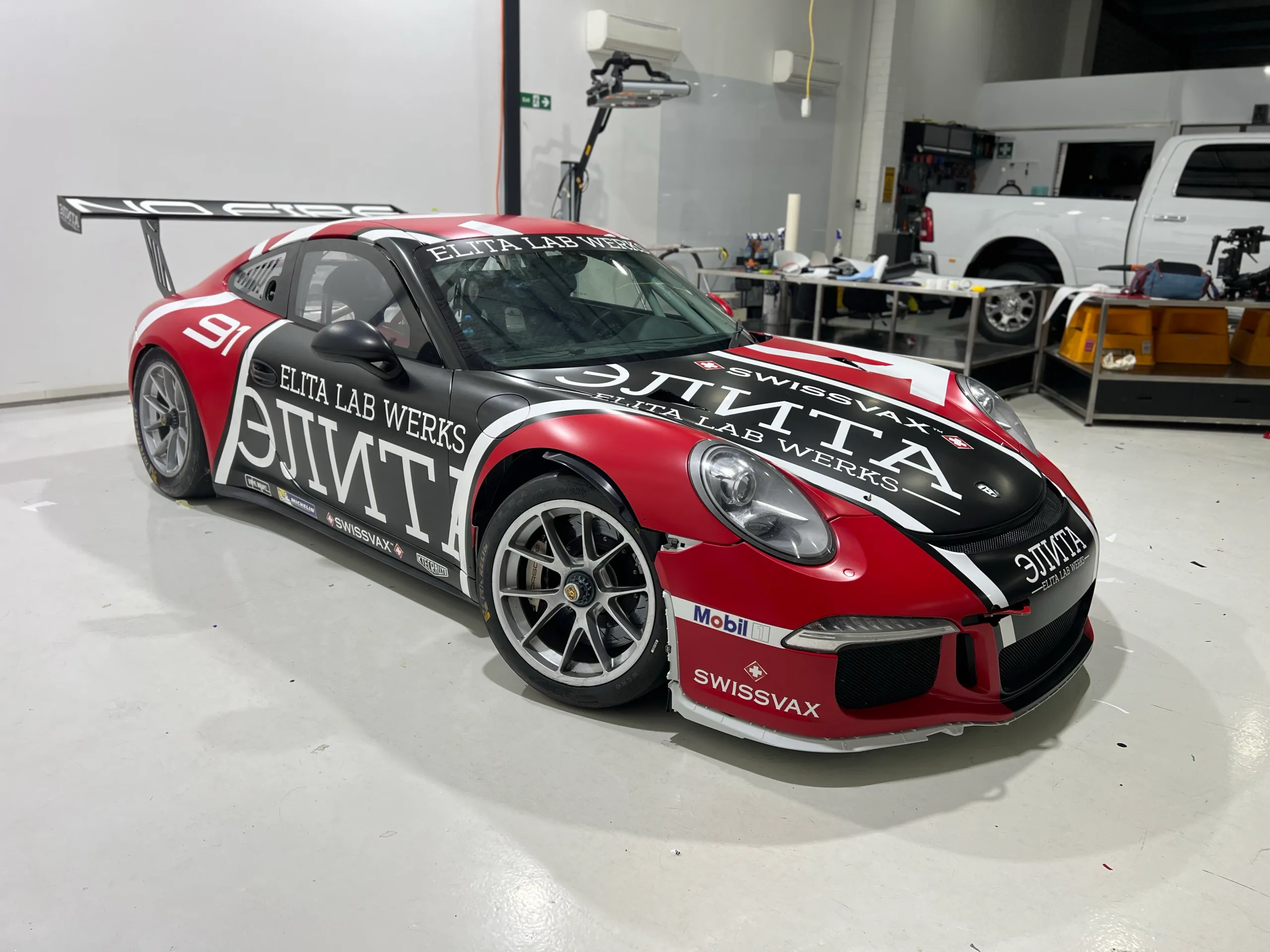 Porsche 911 race car with red, black and white Elita Lab Werks livery and a large rear wing