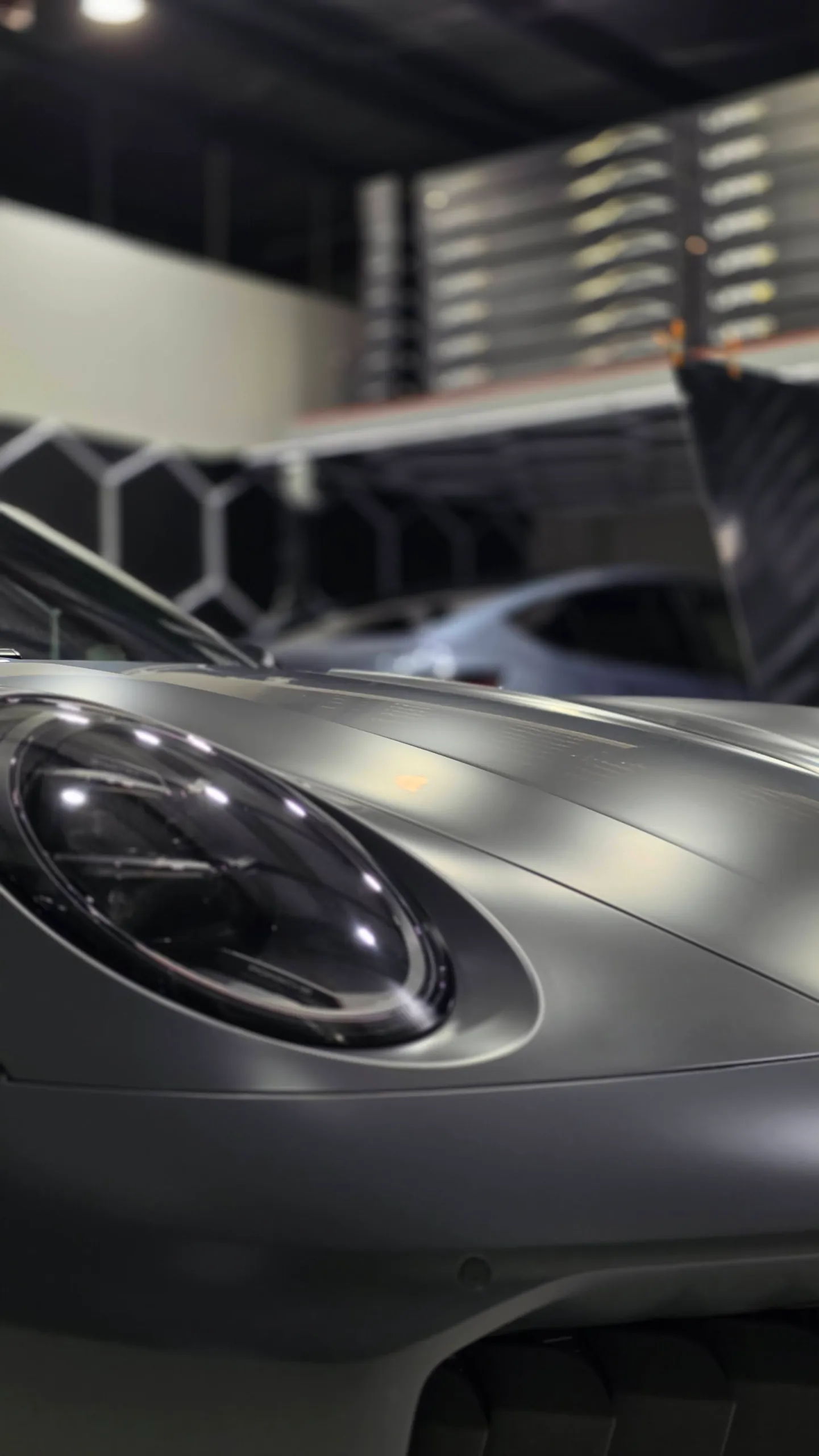Satin grey Porsche 911 bonnet and round headlight beneath workshop lights