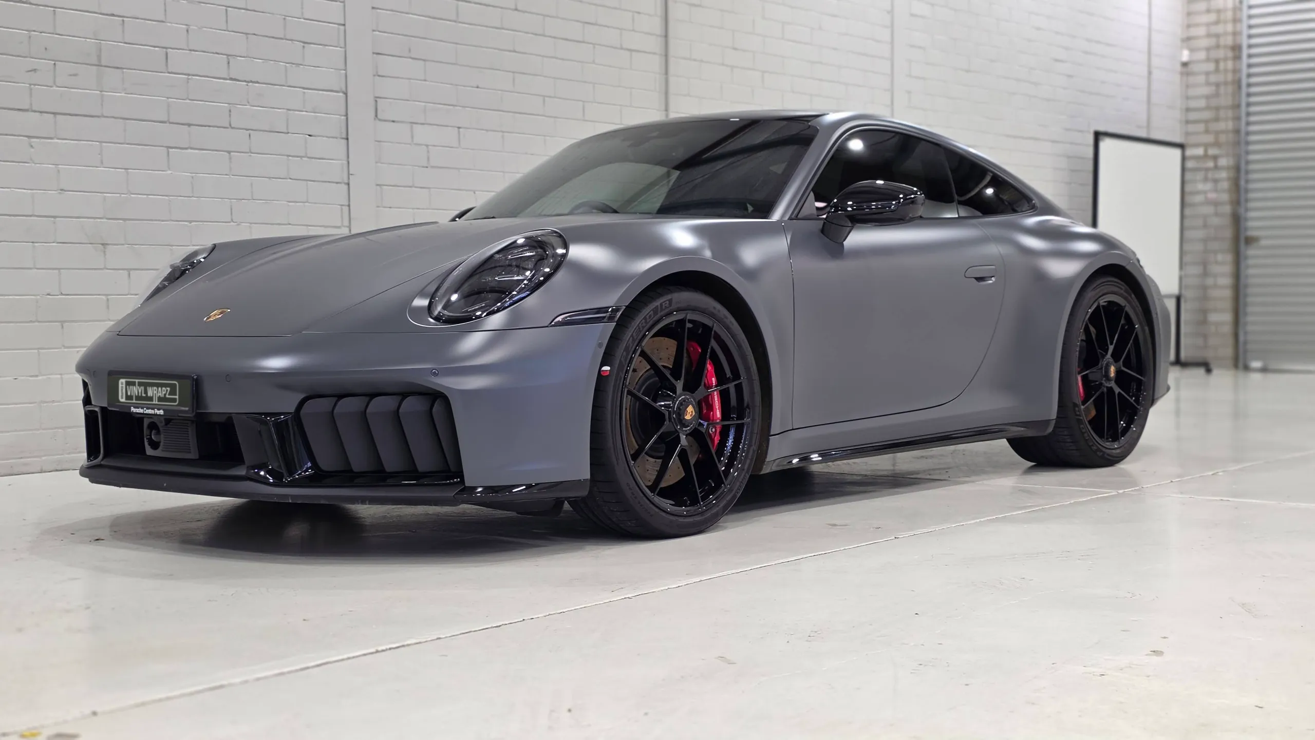 Porsche 911 Carrera GTS with a satin grey finish against a white workshop wall