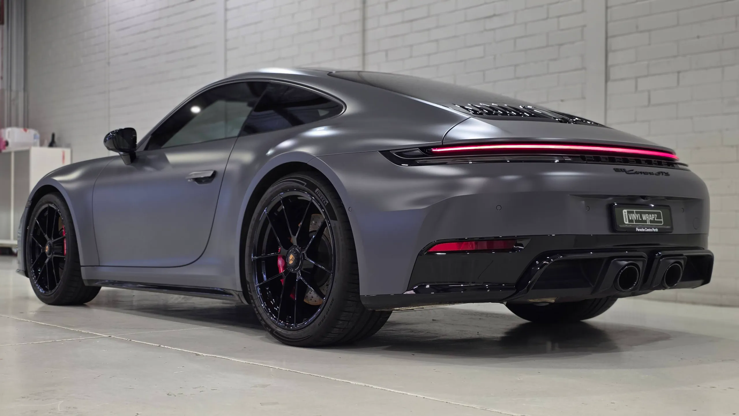Rear-quarter view of the satin grey Porsche 911 Carrera GTS with its rear light bar illuminated