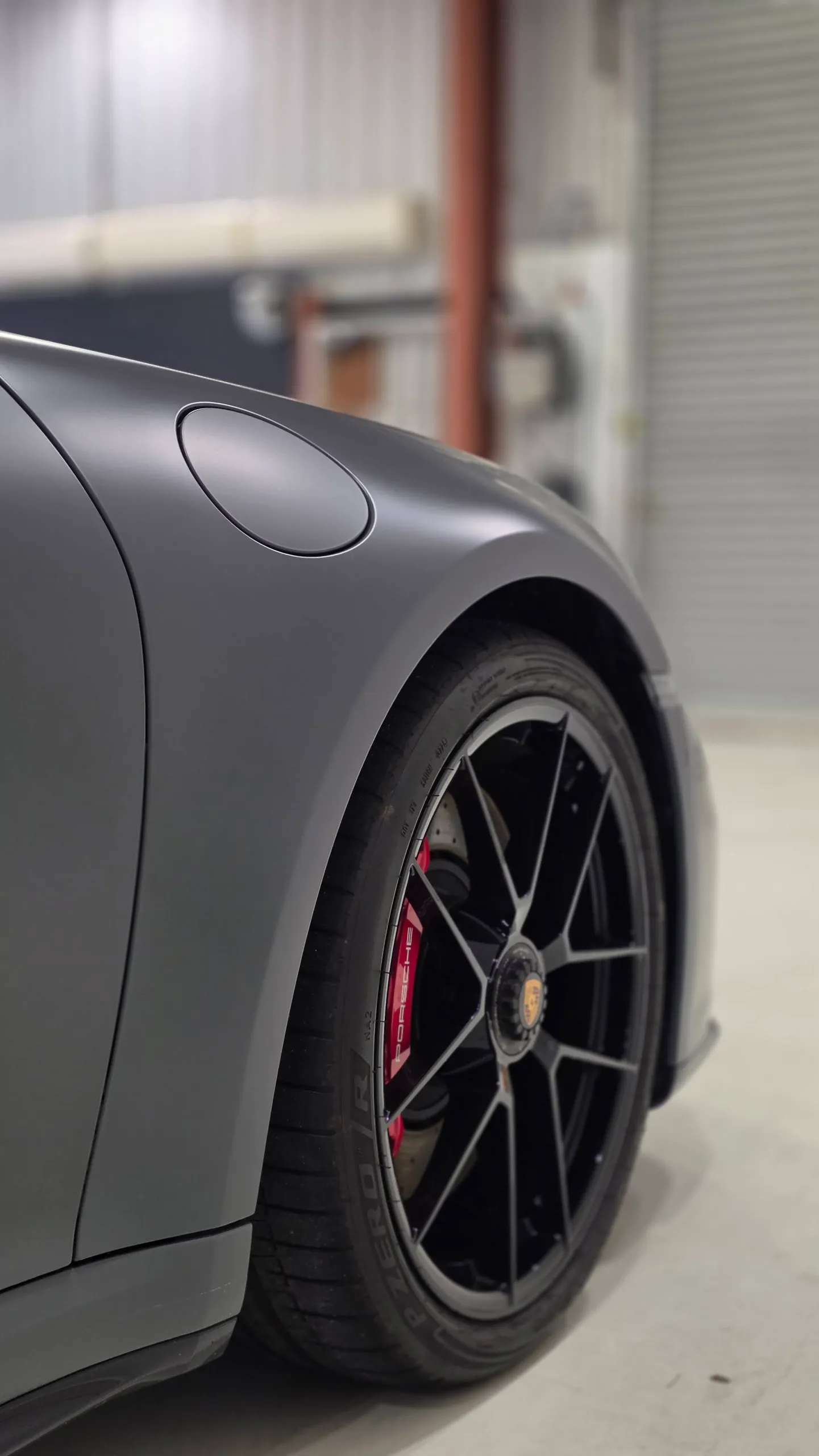 Porsche 911 front wheel and red brake caliper beneath a satin grey guard