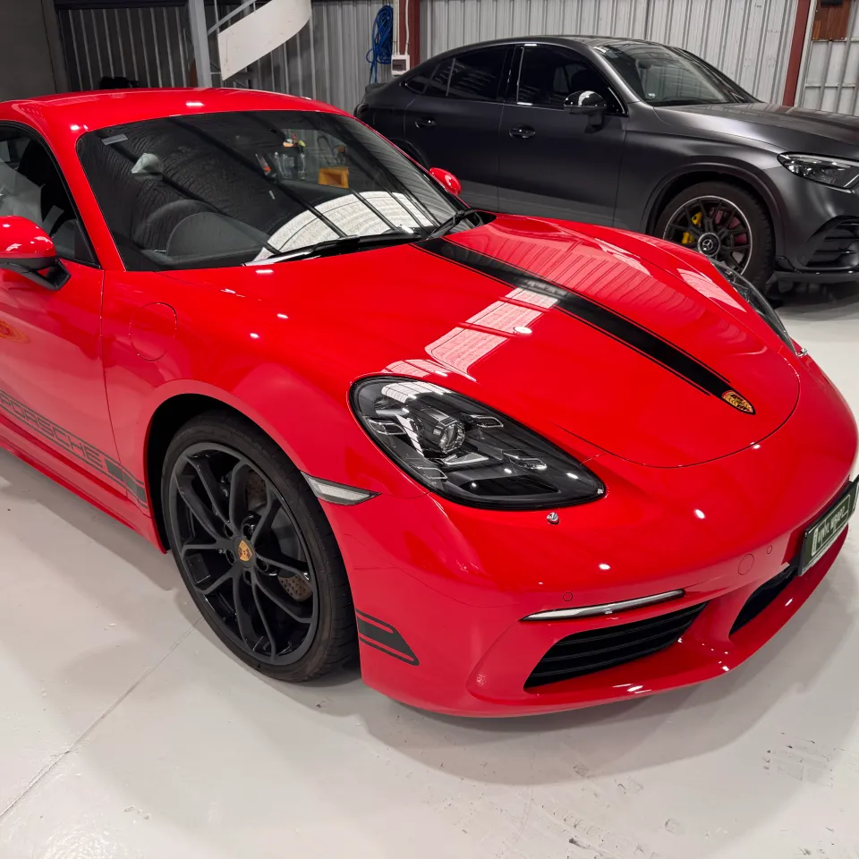 Gloss red Porsche Cayman with black bonnet and side stripes, viewed from the front quarter in the workshop