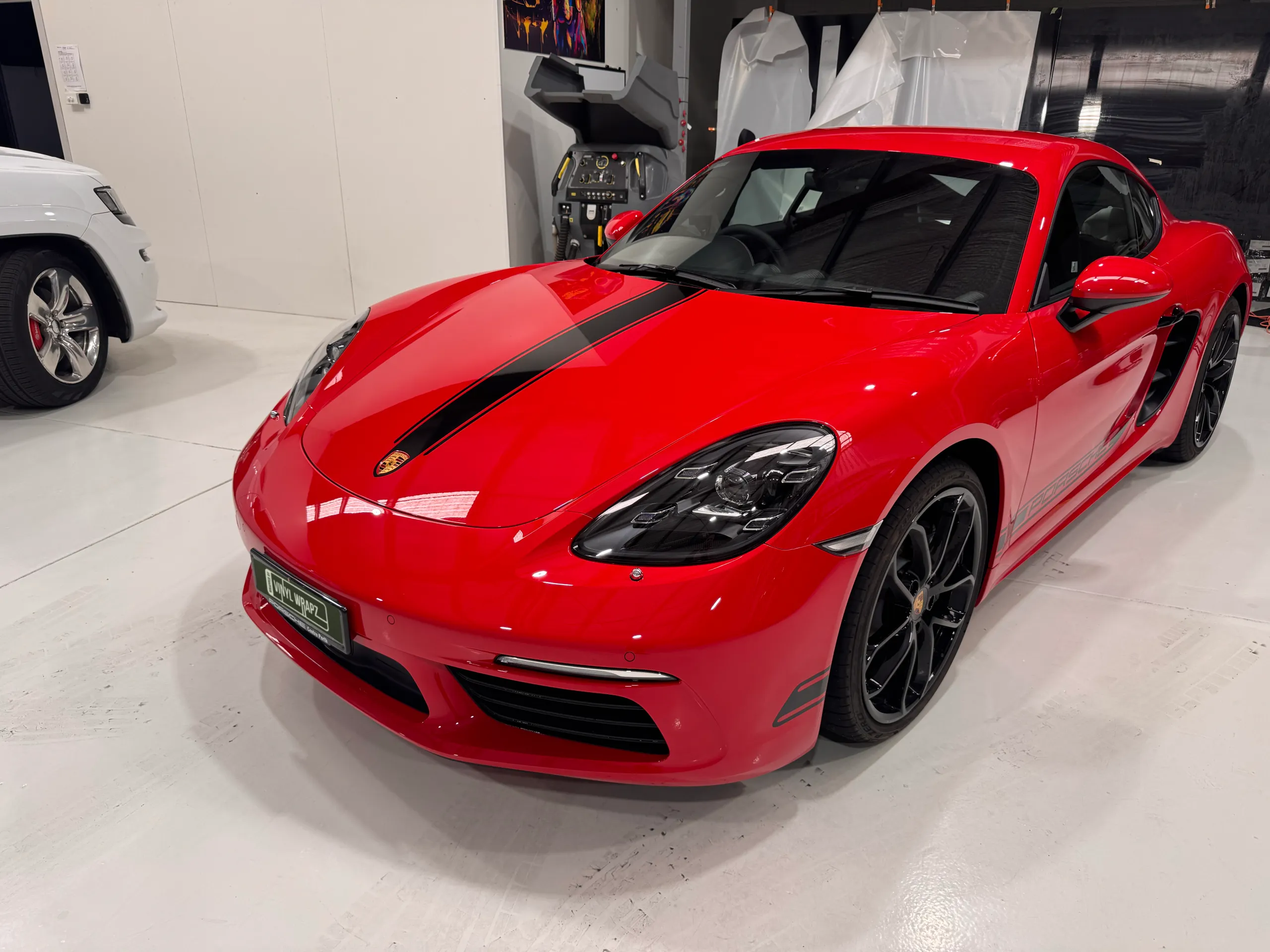 Red Porsche Cayman with black stripes and black wheels in the workshop
