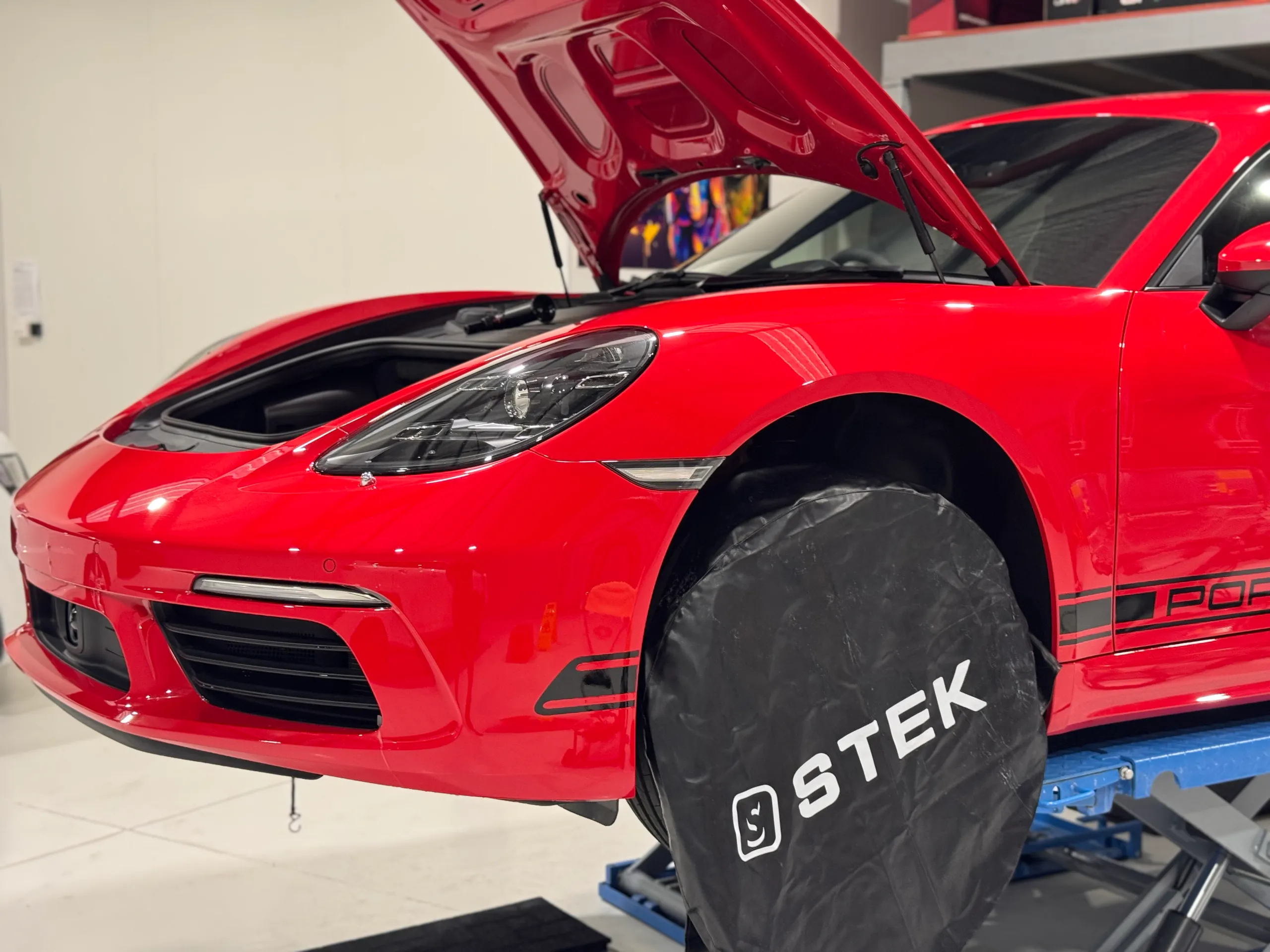 Red Porsche Cayman on a workshop lift with the front luggage compartment open during preparation