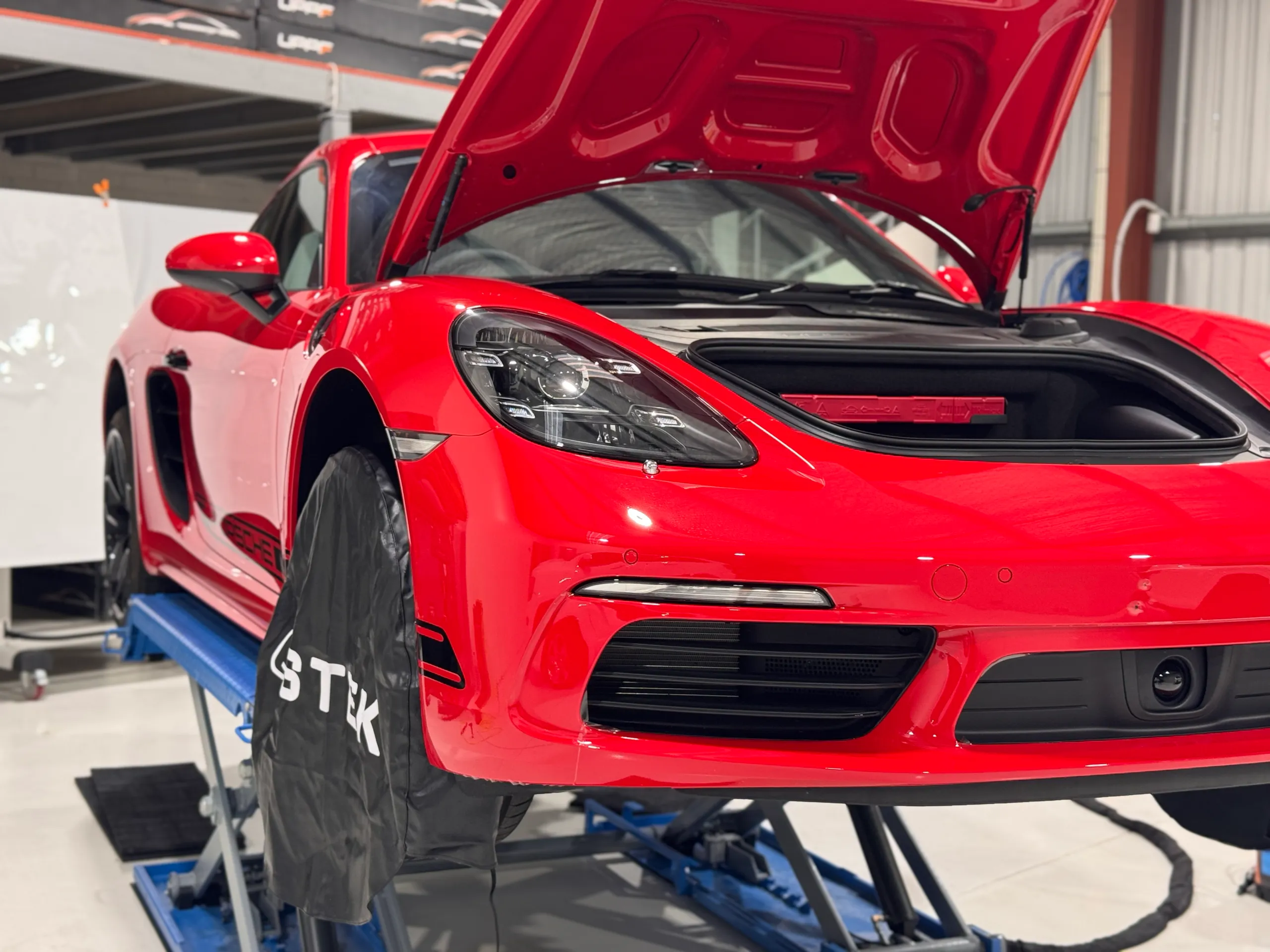 Low front-quarter view of the red Porsche Cayman with its front luggage compartment open