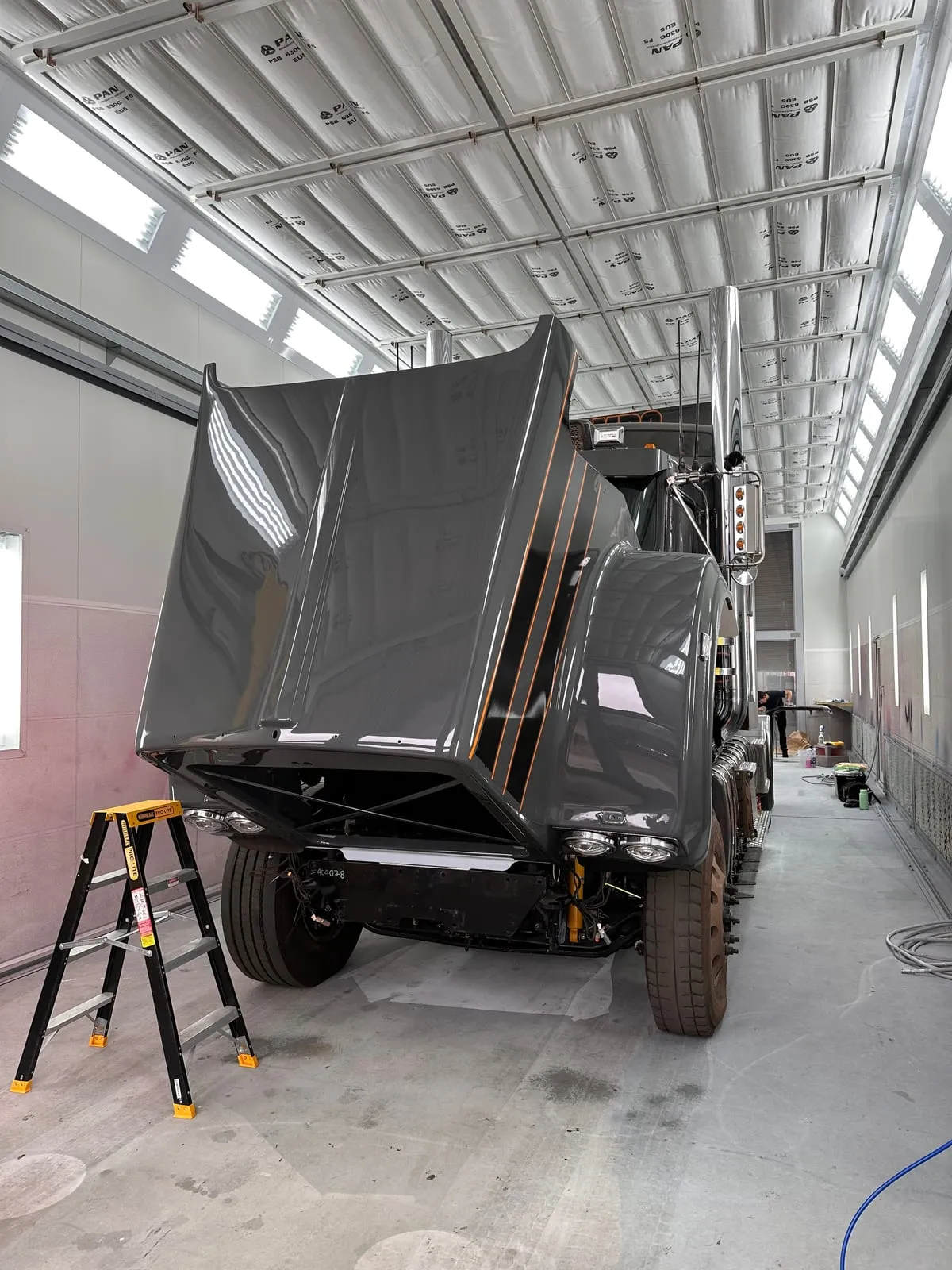 A grey prime mover with the bonnet raised inside the fleet workshop bay, with orange pinstripe accents along the cab
