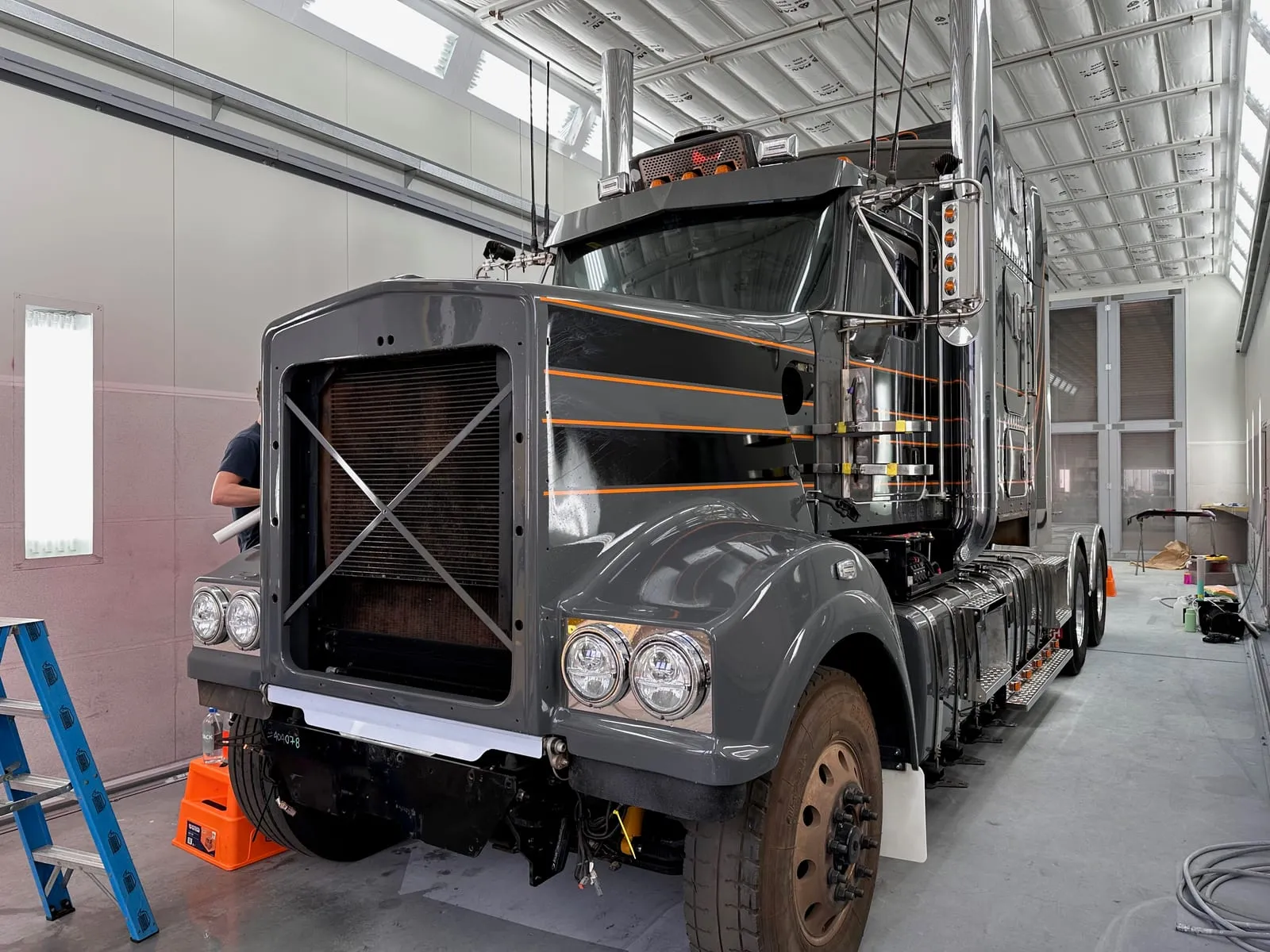 Grey prime mover with orange pinstripe accents parked front on inside the fleet workshop