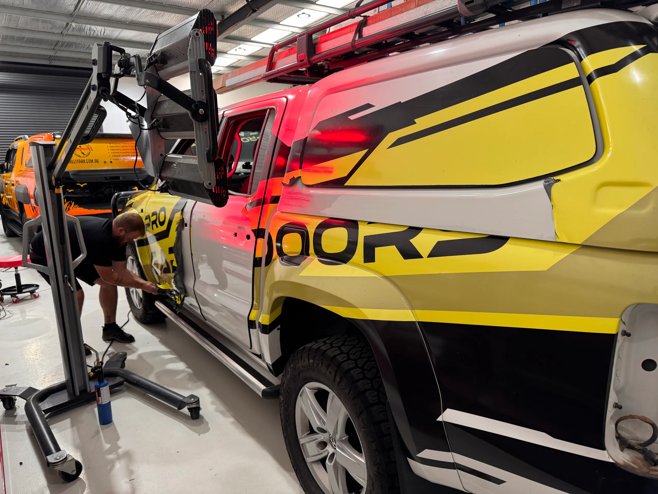 Installer fitting yellow and black Pro Garage Doors graphics to a Volkswagen Amarok door