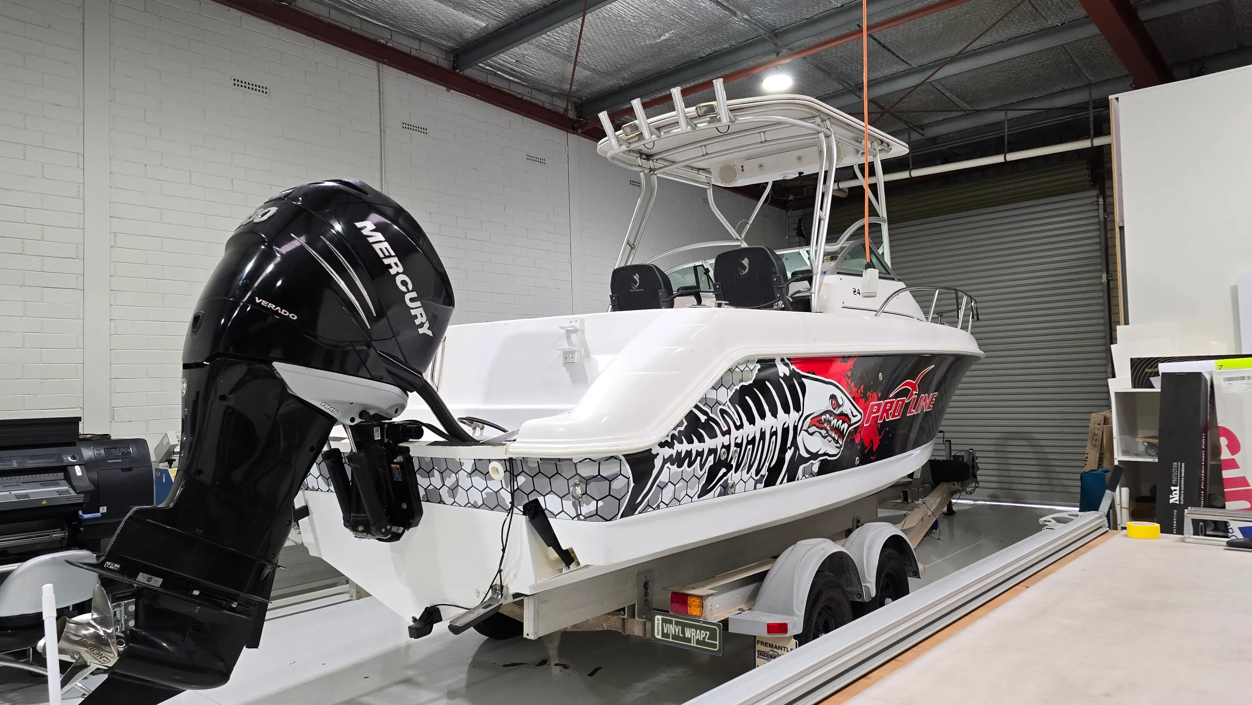 Pro-Line boat stern quarter with shark graphics and a black Mercury outboard in the workshop