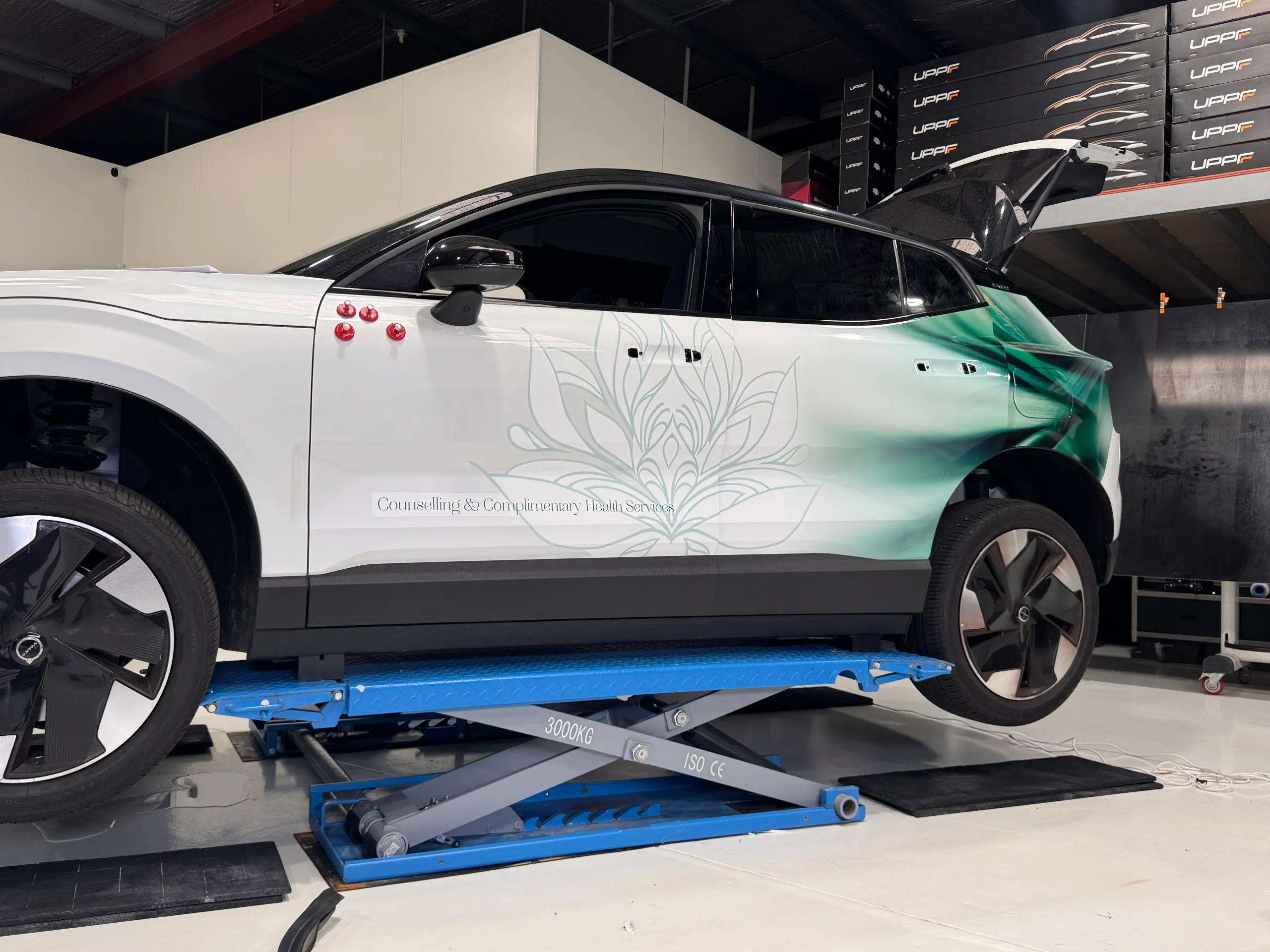 Green and white Puresoul Wellness graphics being fitted to a Volvo on a workshop lift