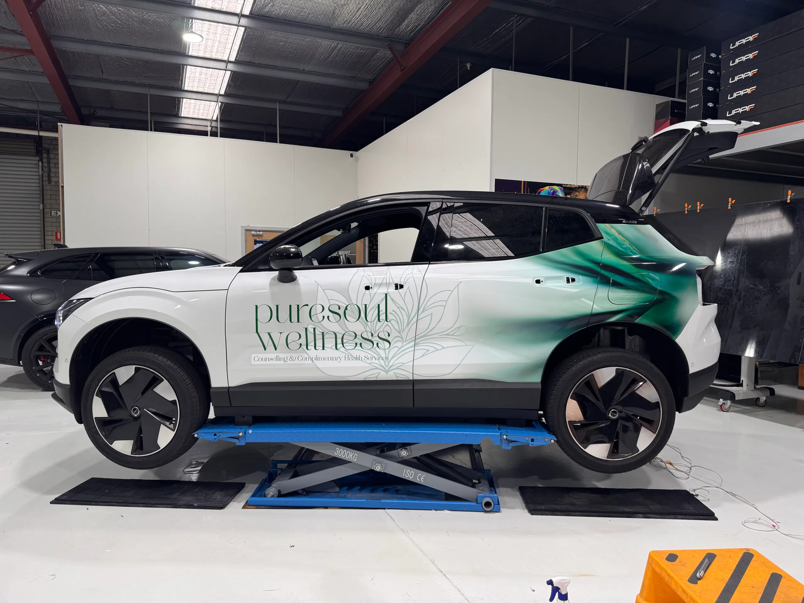 Volvo on a workshop lift during Puresoul Wellness branding, with door handles removed