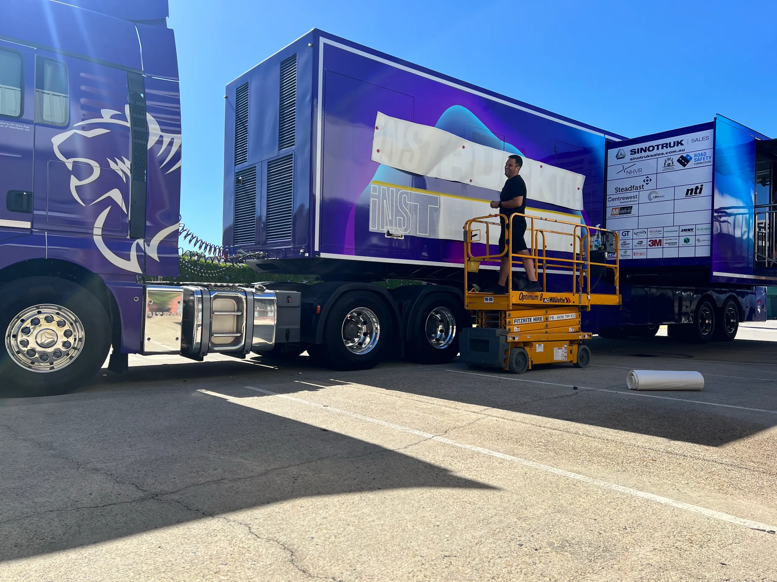 Installer fitting trailer graphics from an elevated platform