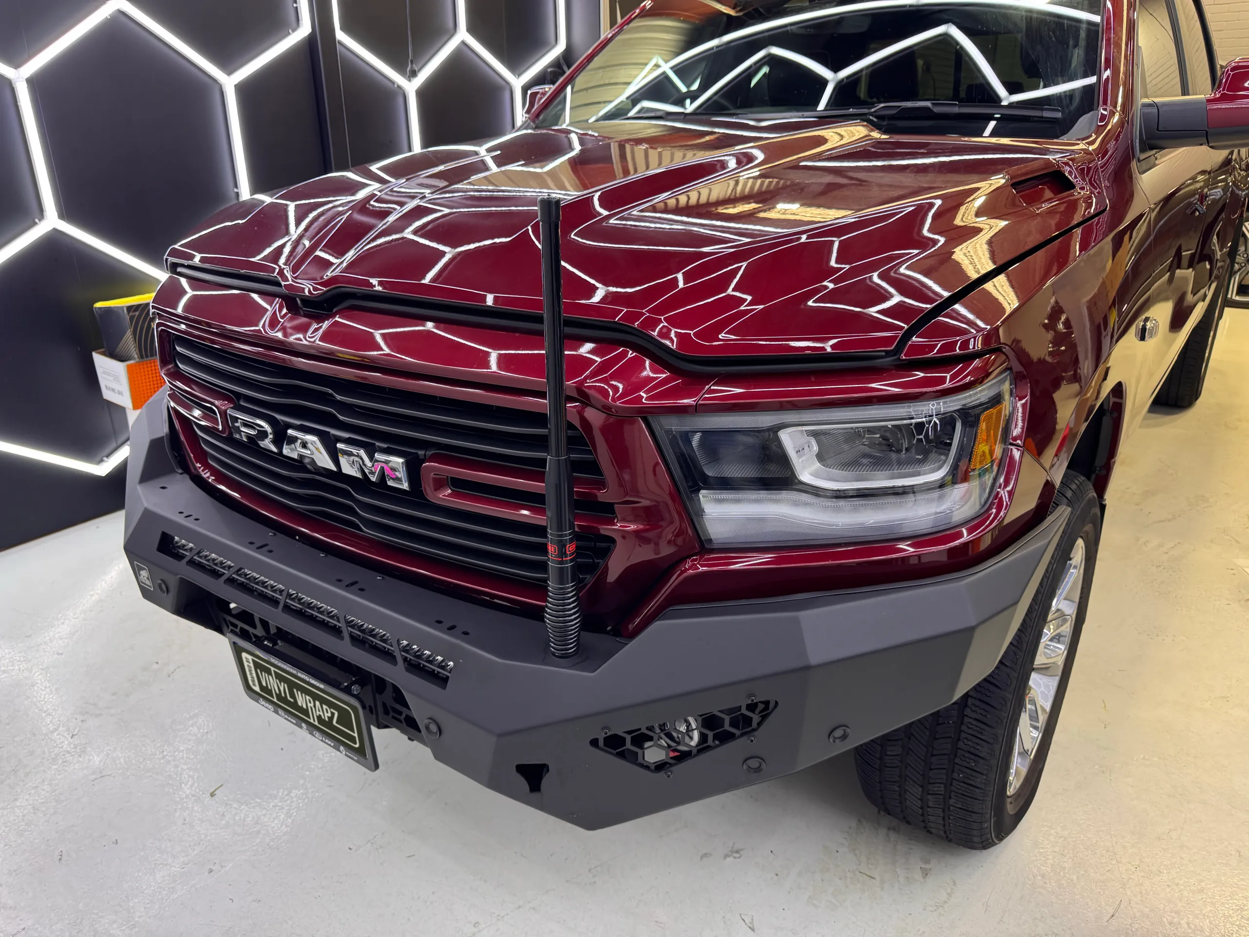 Gloss dark red Ram 1500 front end in the workshop, with a steel bumper and the bonnet slightly raised