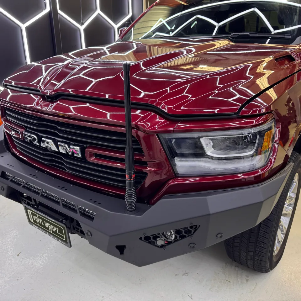 Gloss dark red Ram 1500 front end in the workshop, with a steel bumper and the bonnet slightly raised