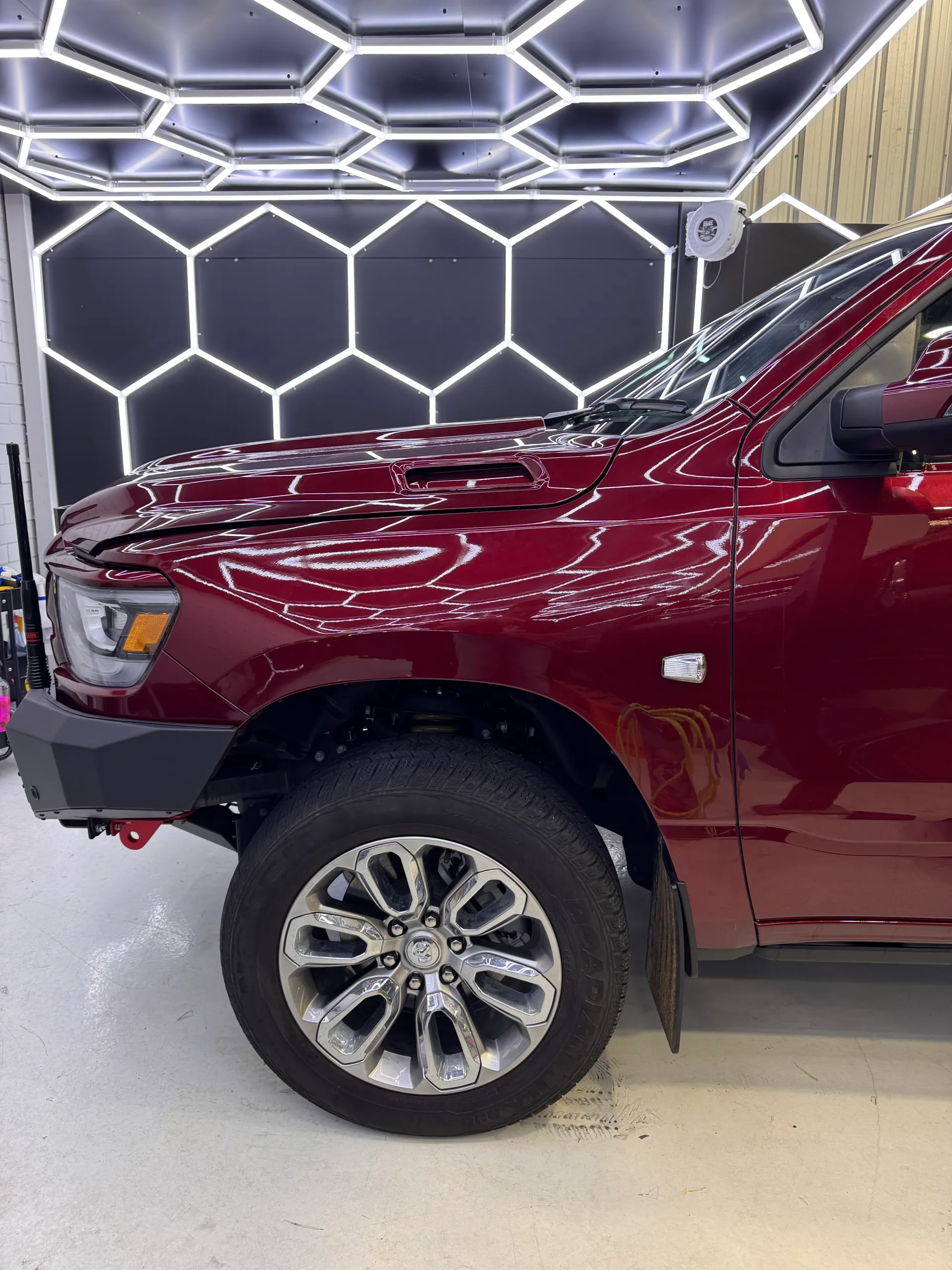 Dark red Ram 1500 front wheel and guard beneath reflected workshop lights