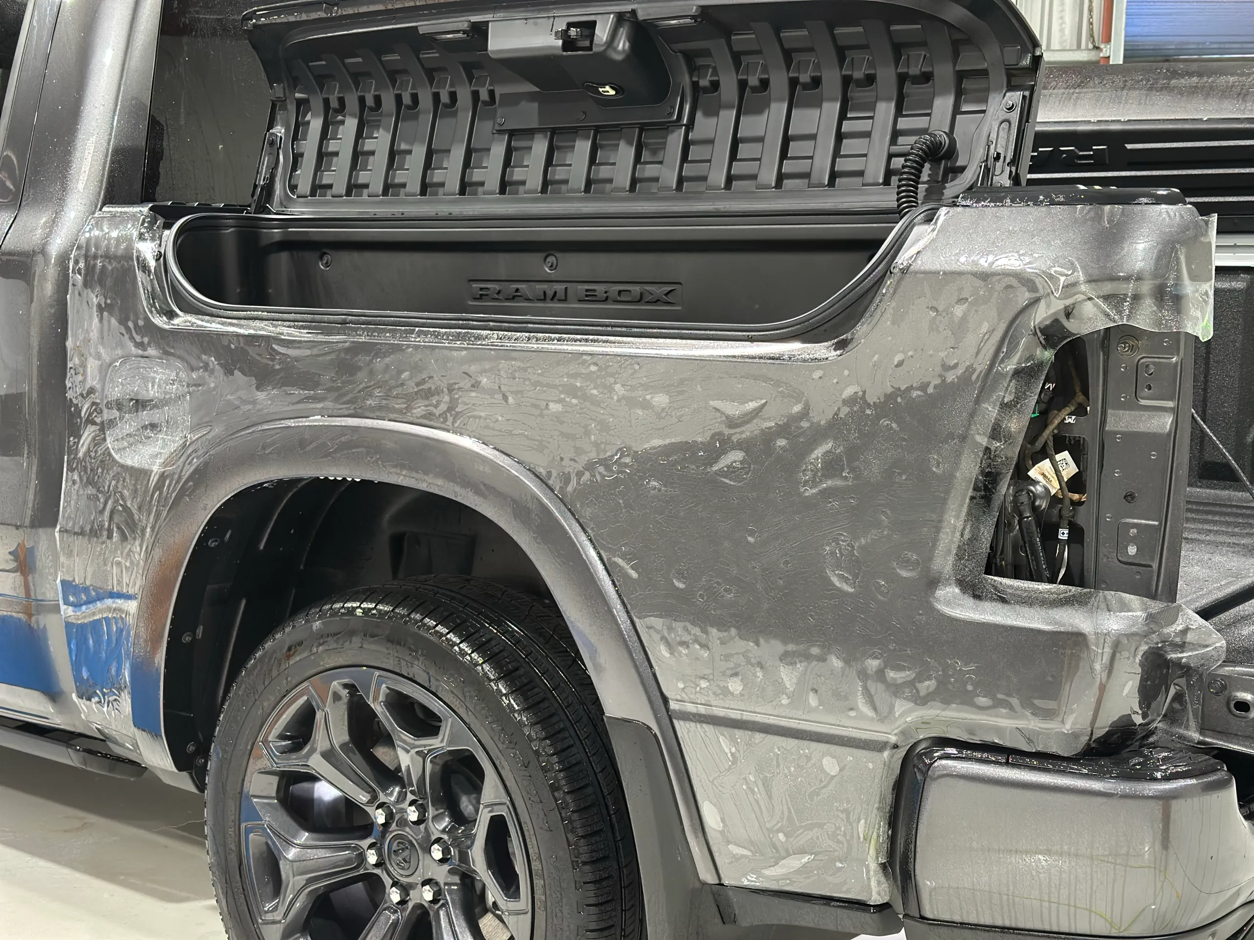 Clear film on the grey Ram 1500 rear quarter during installation, with the RamBox open and rear light removed
