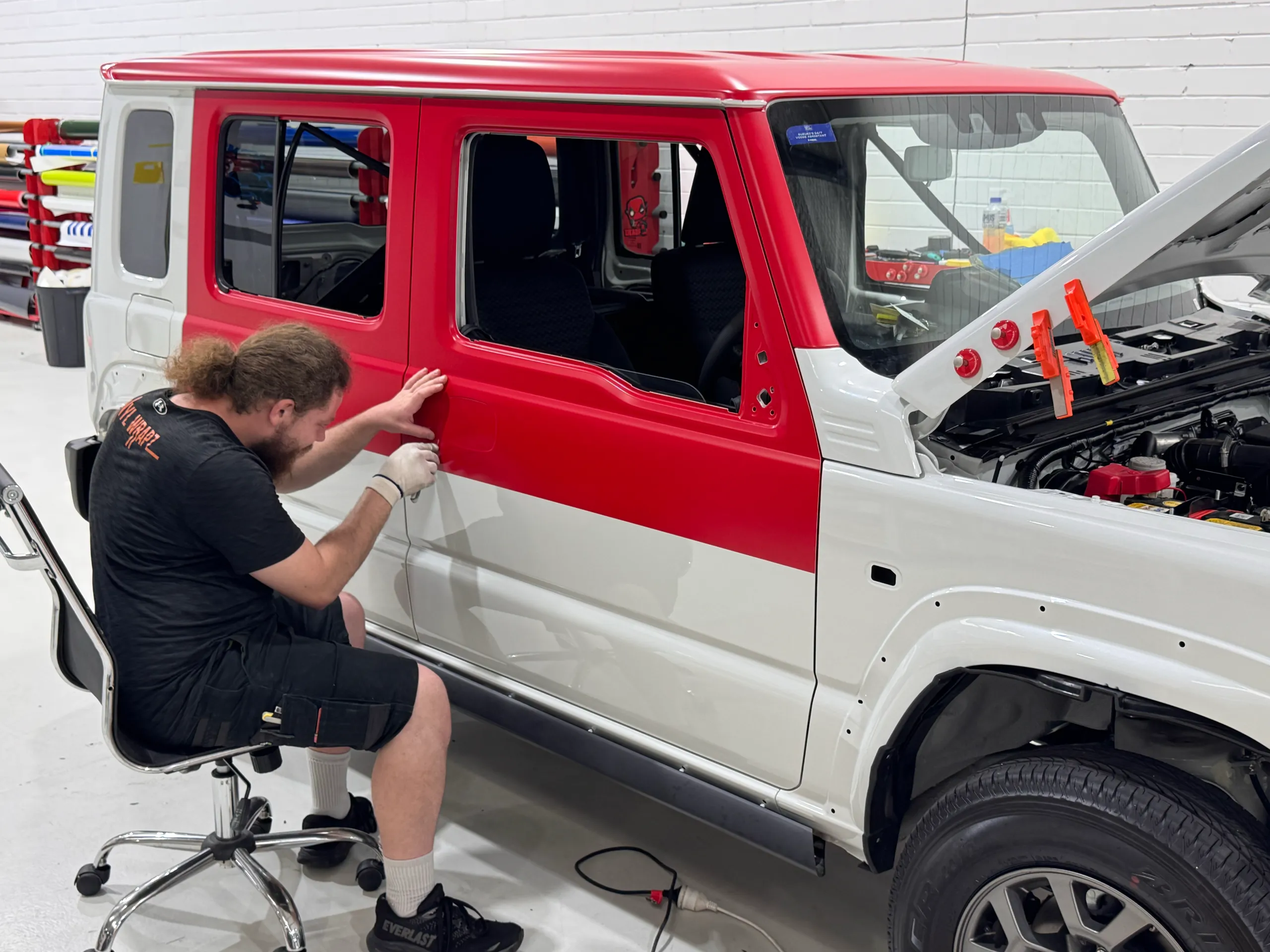 Installer trimming red film across the Suzuki Jimny door during wrapping
