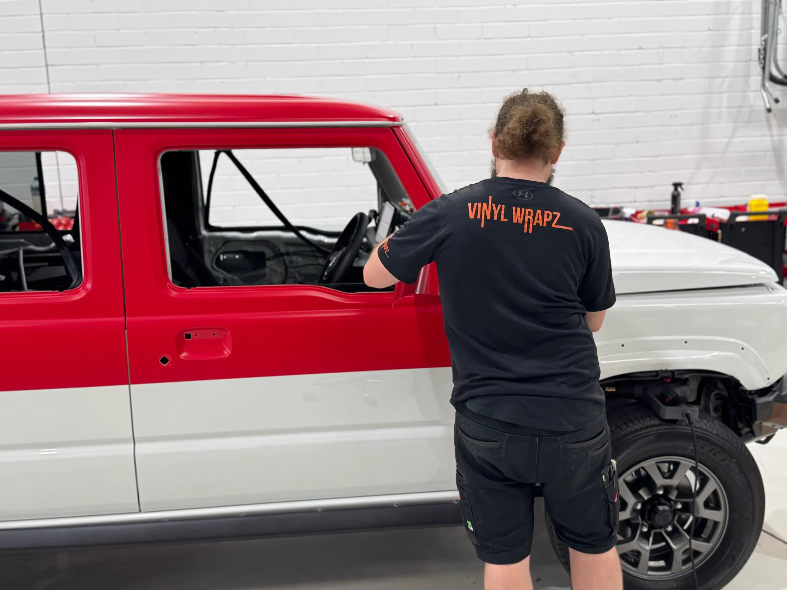 Back-facing installer working on the Jimny side with red upper panels and white lower panels