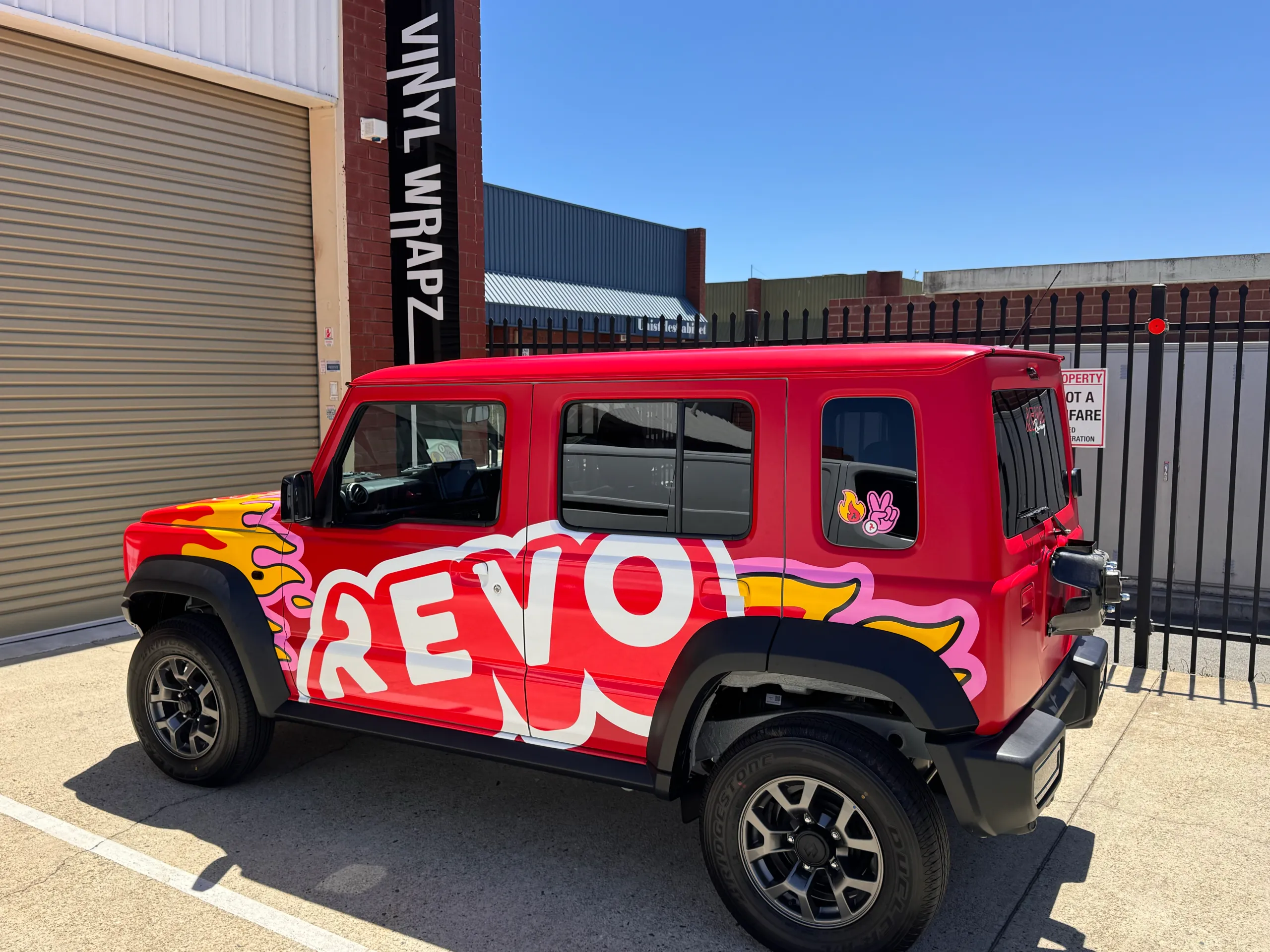 Red Suzuki Jimny with Revo side graphics outside the workshop, with its spare wheel removed