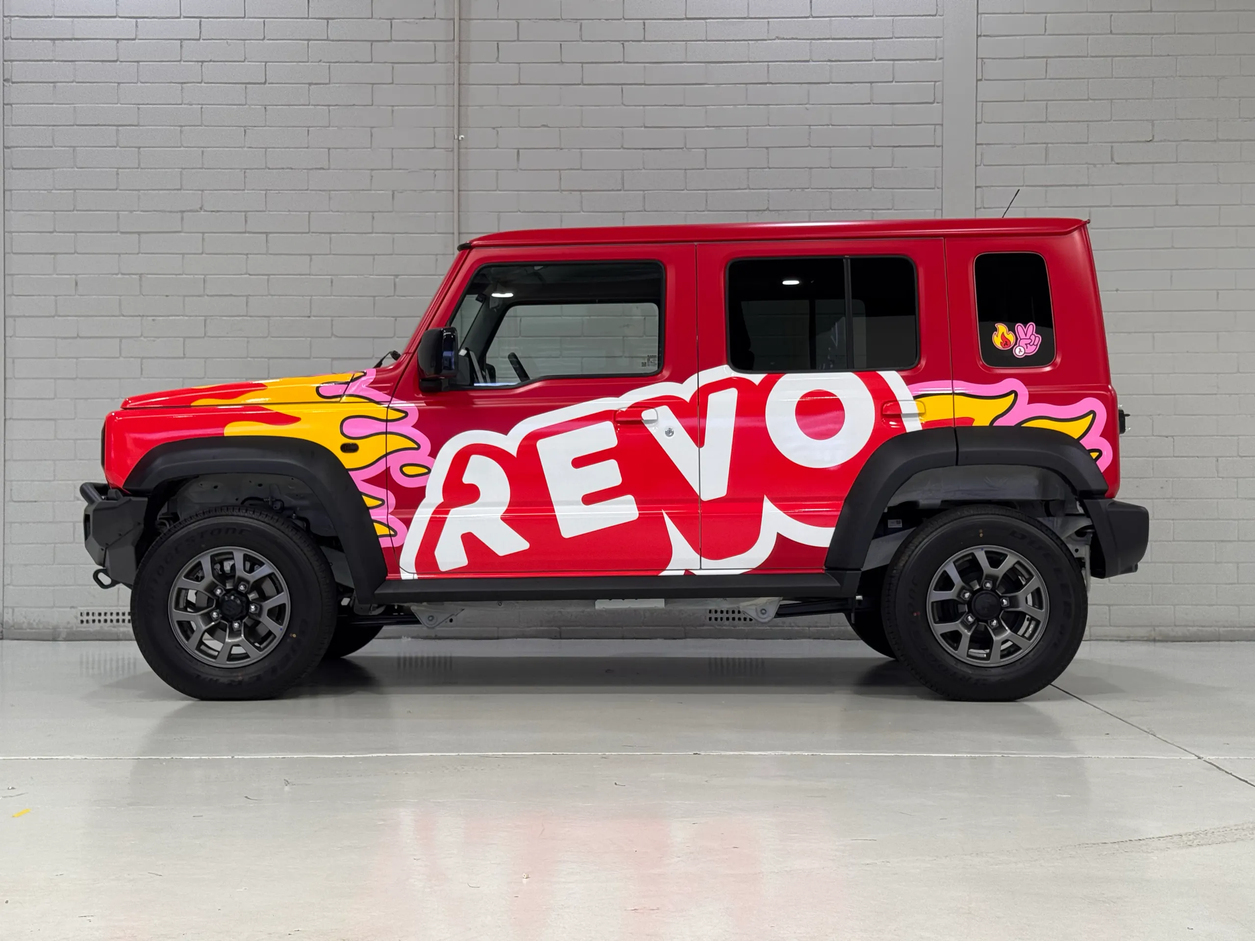 Side profile of the red Suzuki Jimny with white Revo lettering and flame graphics