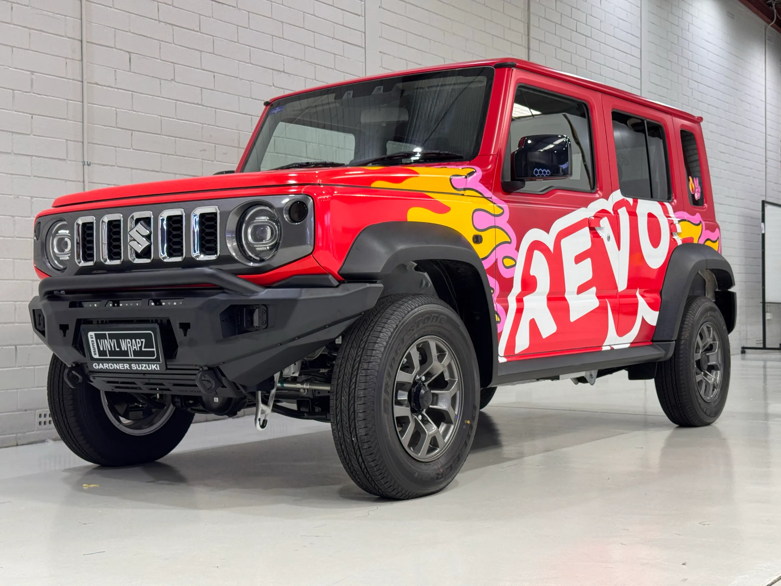 Low front-quarter view of the red Revo Suzuki Jimny inside the workshop