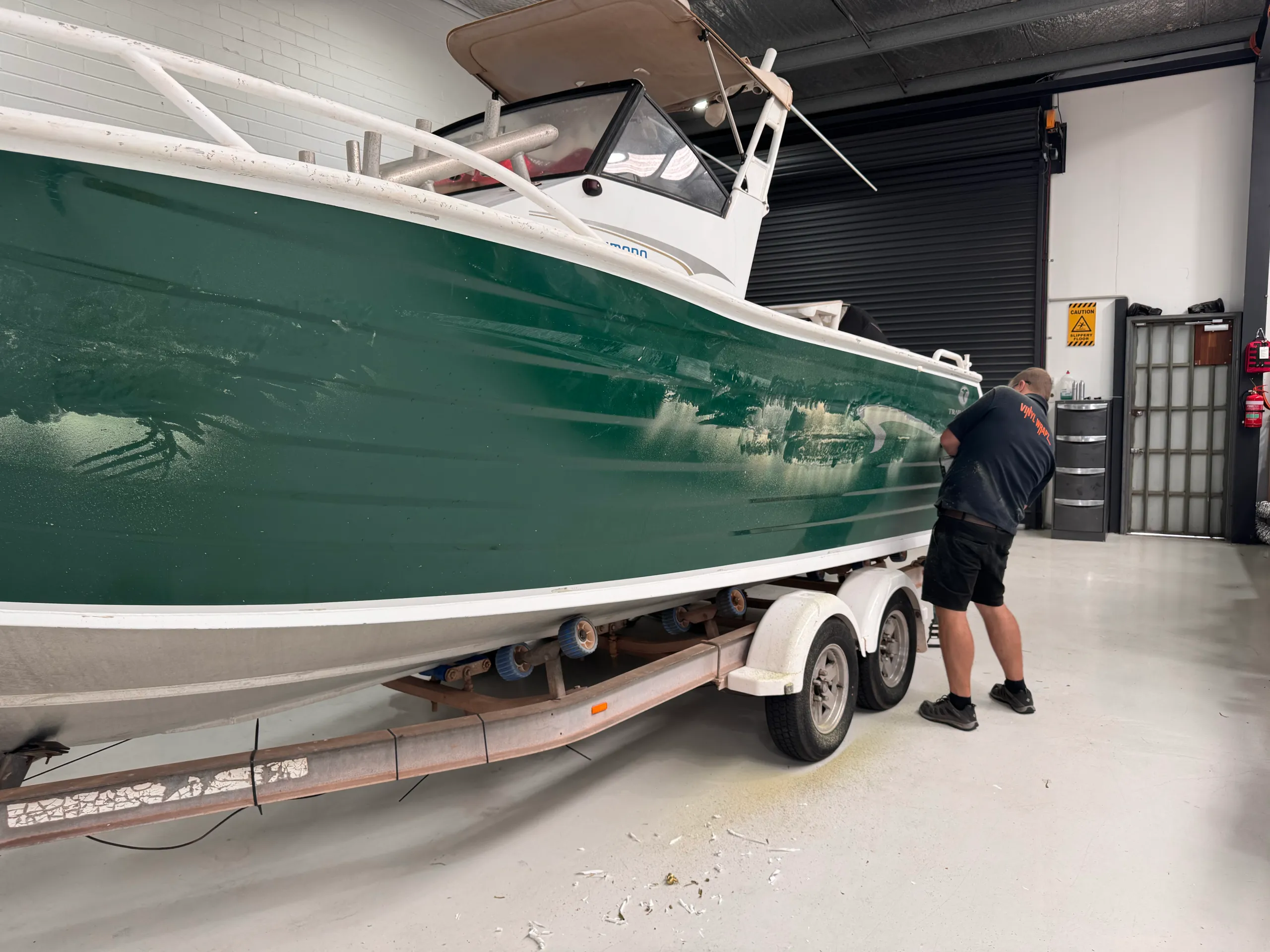 Installer preparing the scuffed green hull near the stern, with their back to the camera