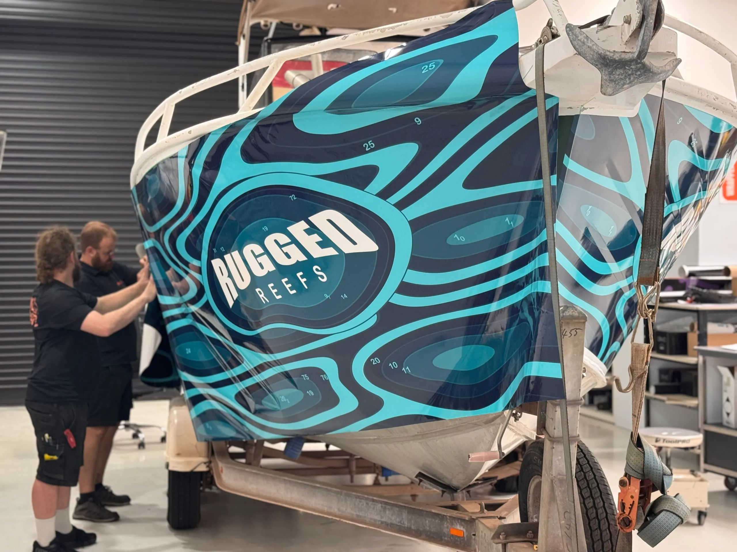 Installers smoothing the teal graphic wrap around the boat bow