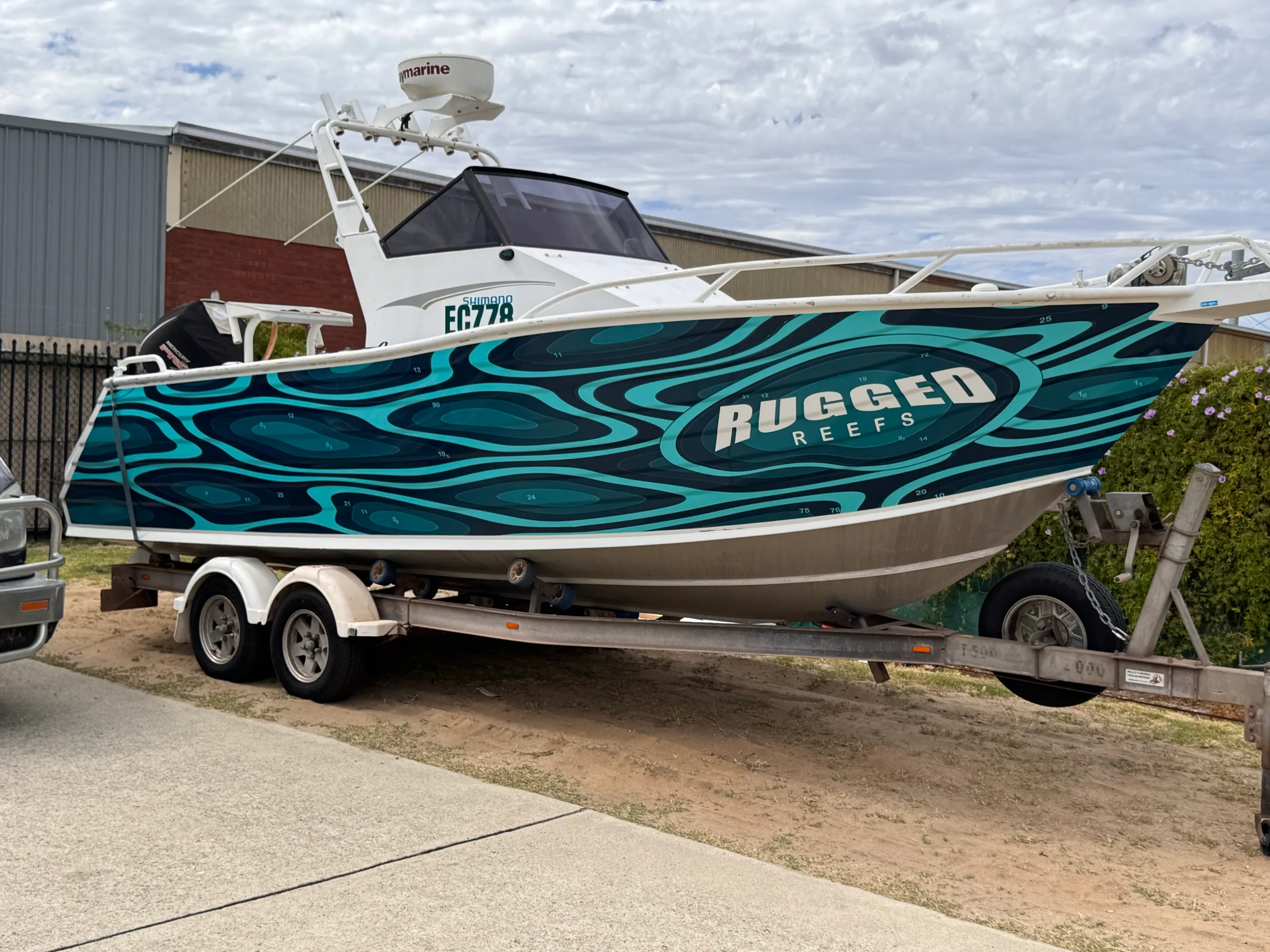 Rugged Reefs teal hull graphics on the boat outside beside a hedge