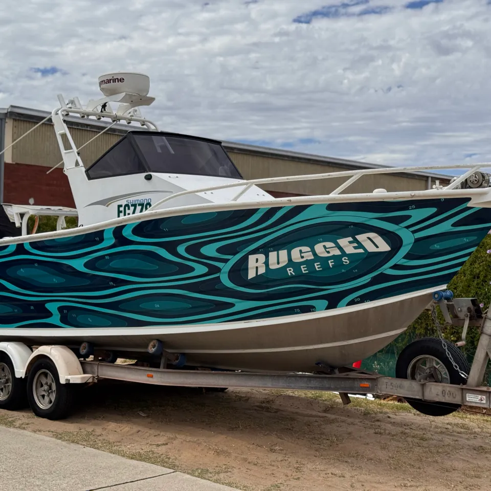 Teal Rugged Reefs boat on its trailer outdoors under a cloudy sky