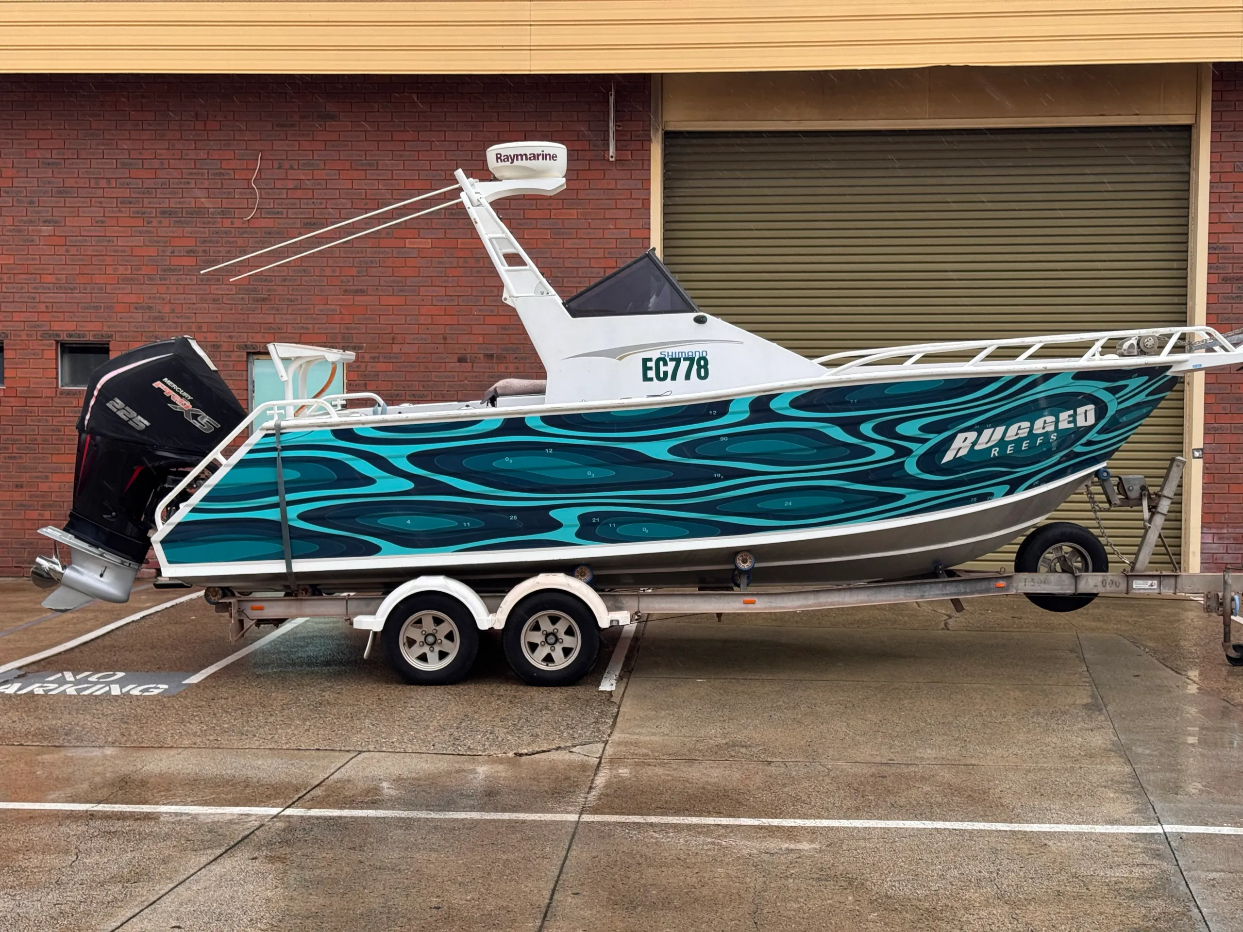 Rugged Reefs boat and trailer outside a brick building on wet pavement