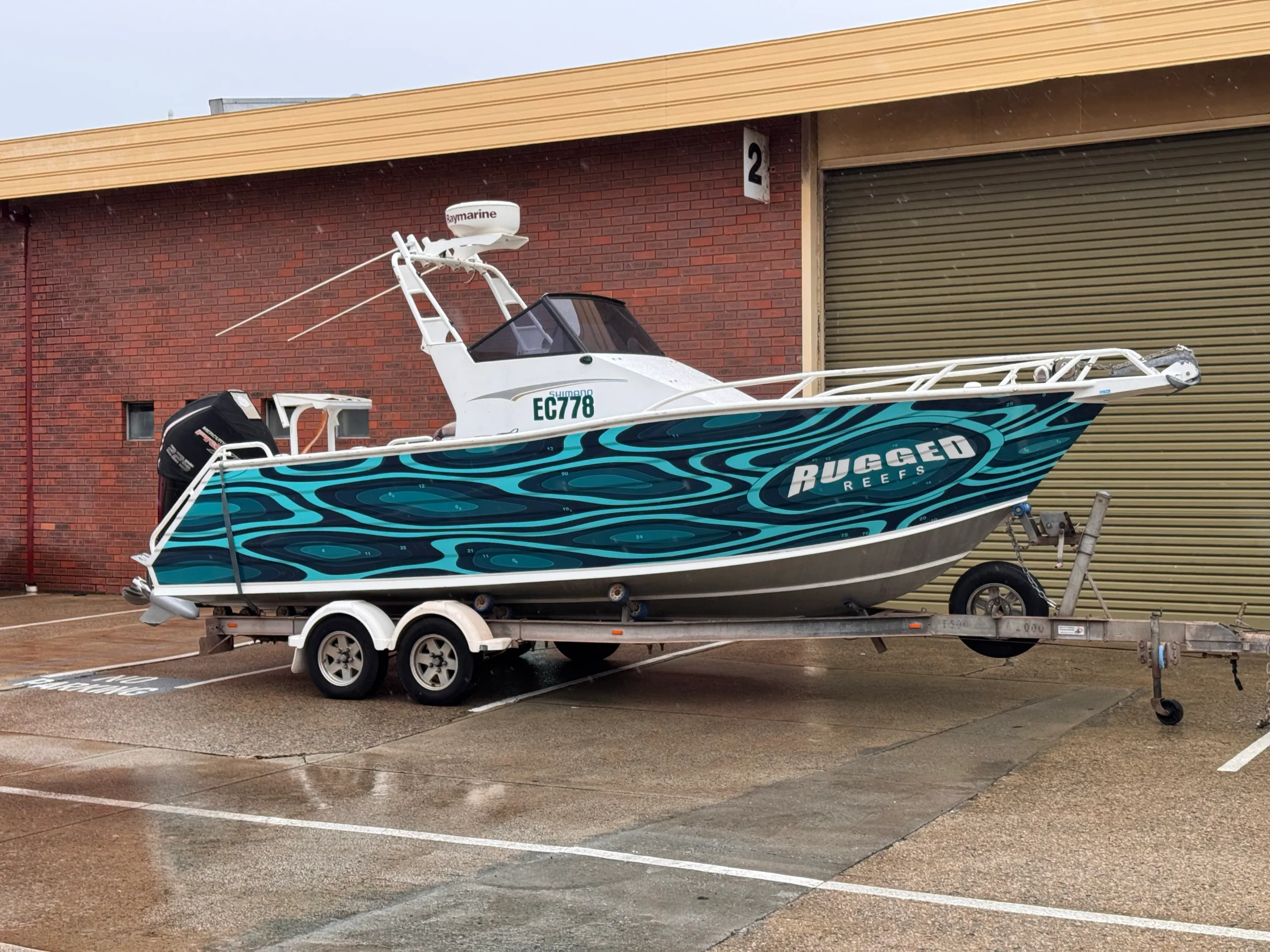 Wide view of the completed teal Rugged Reefs boat and trailer outside the workshop