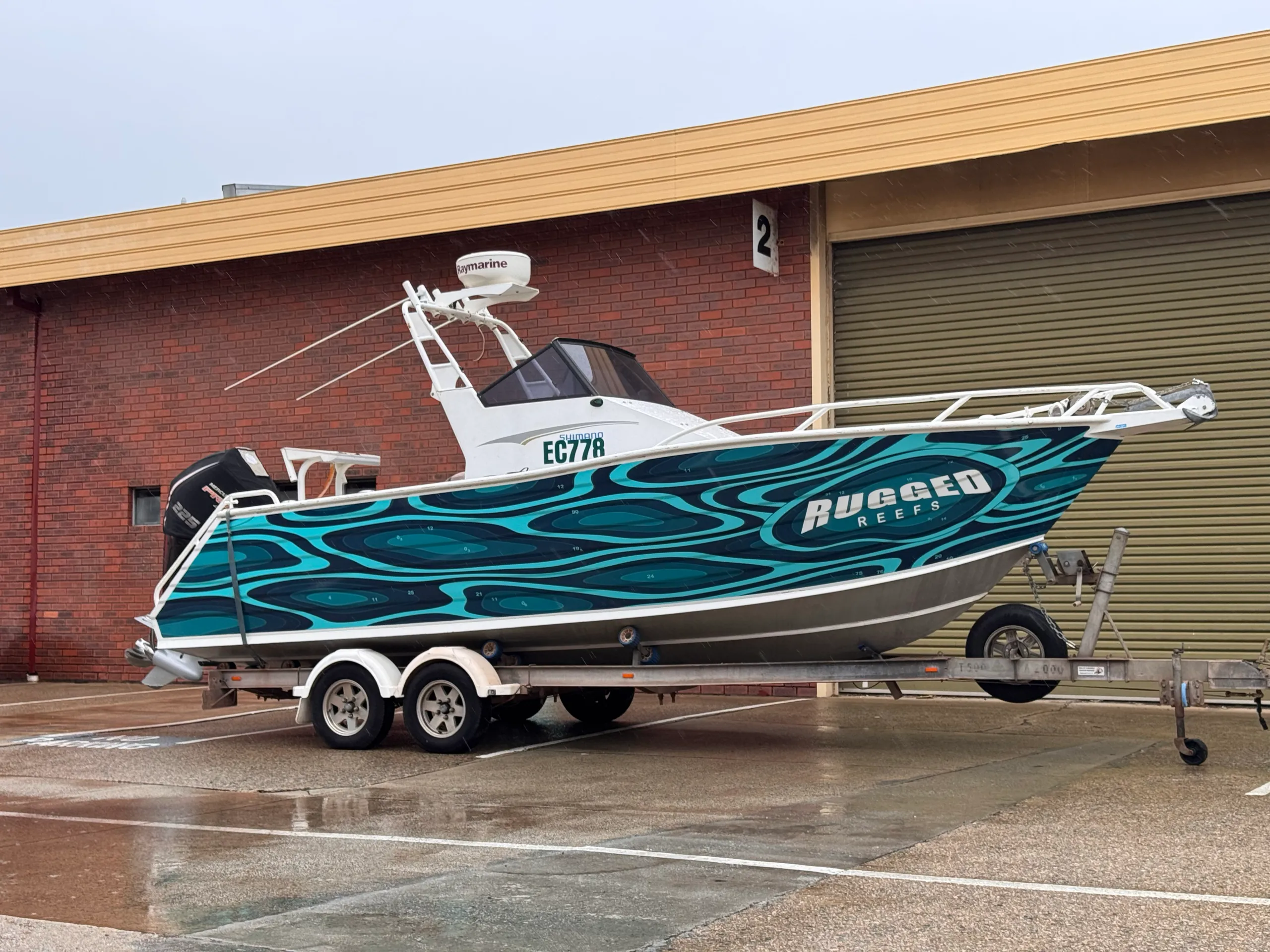Angled photograph of the Rugged Reefs boat and trailer outside on wet pavement