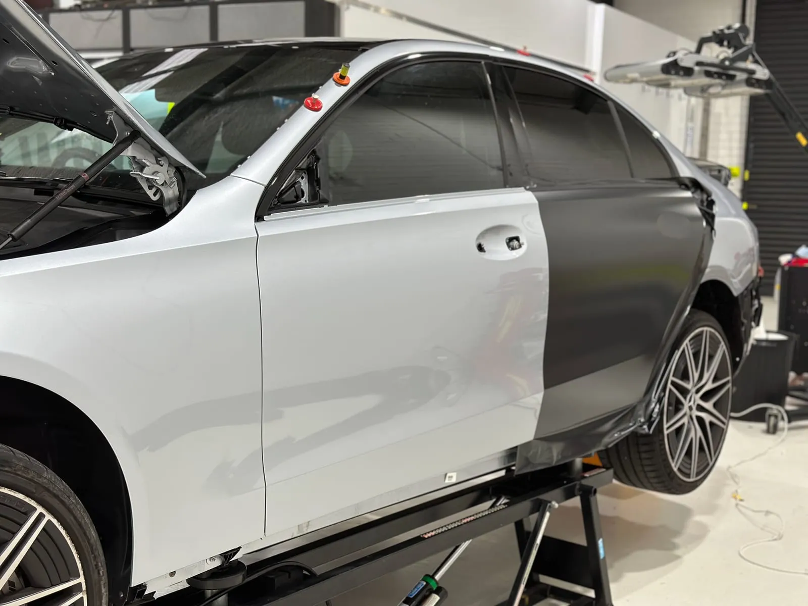 Silver sedan raised on a hoist with satin gunmetal wrap film applied to the rear door and quarter panel