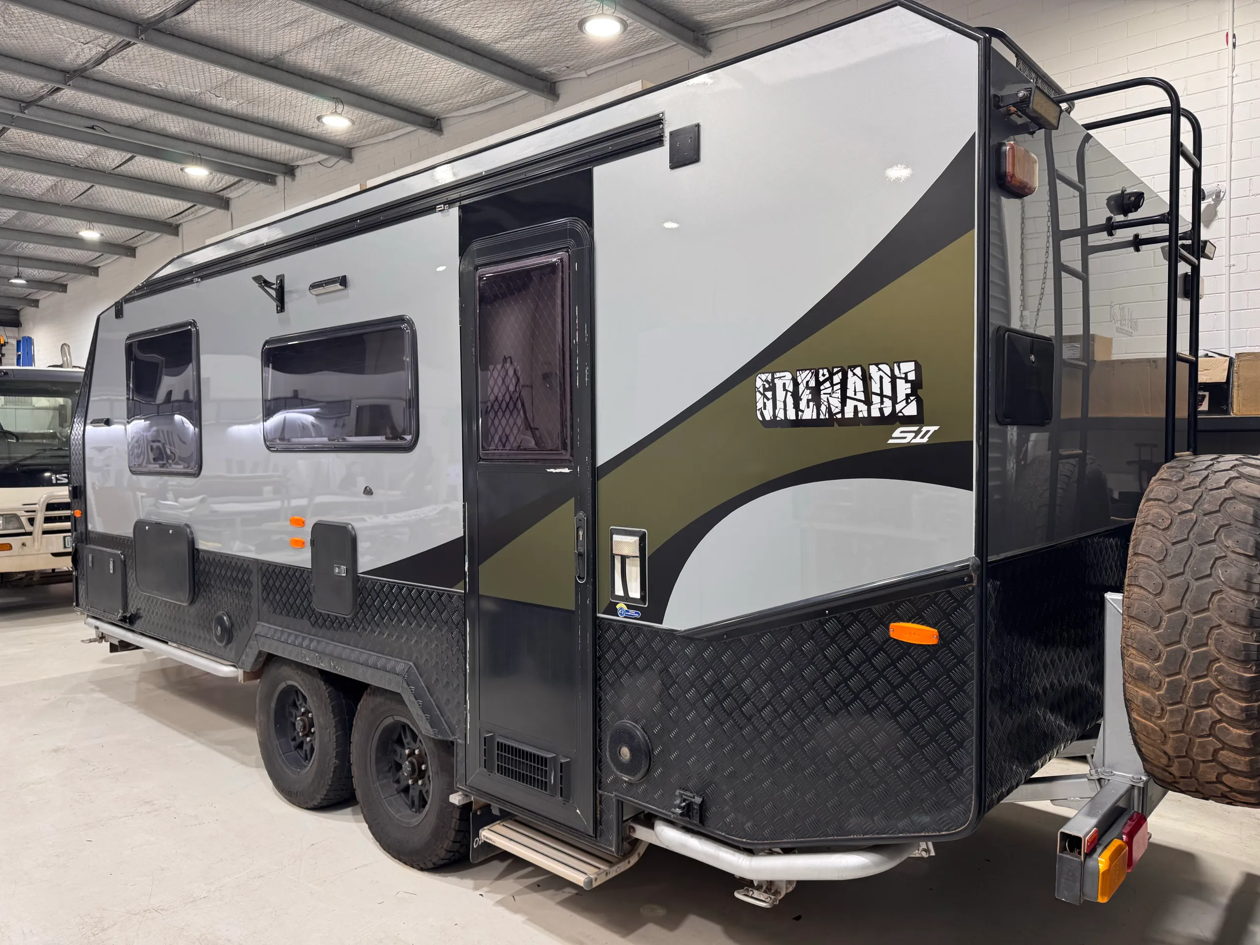 Silver caravan with olive green and black side graphics in the workshop
