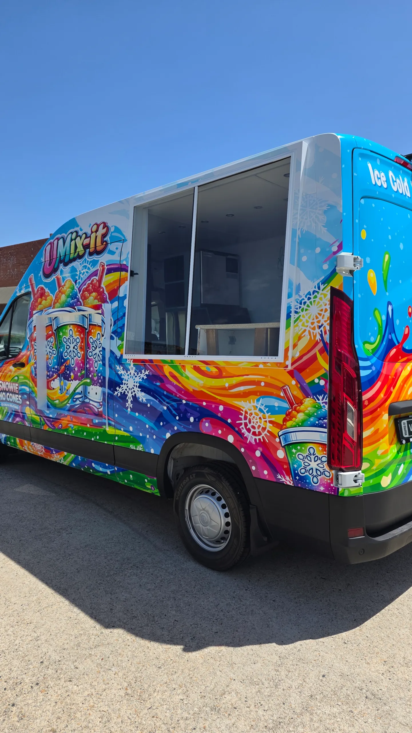 Colourfully wrapped Snowie Sno Cones van showing the serving window and rear corner