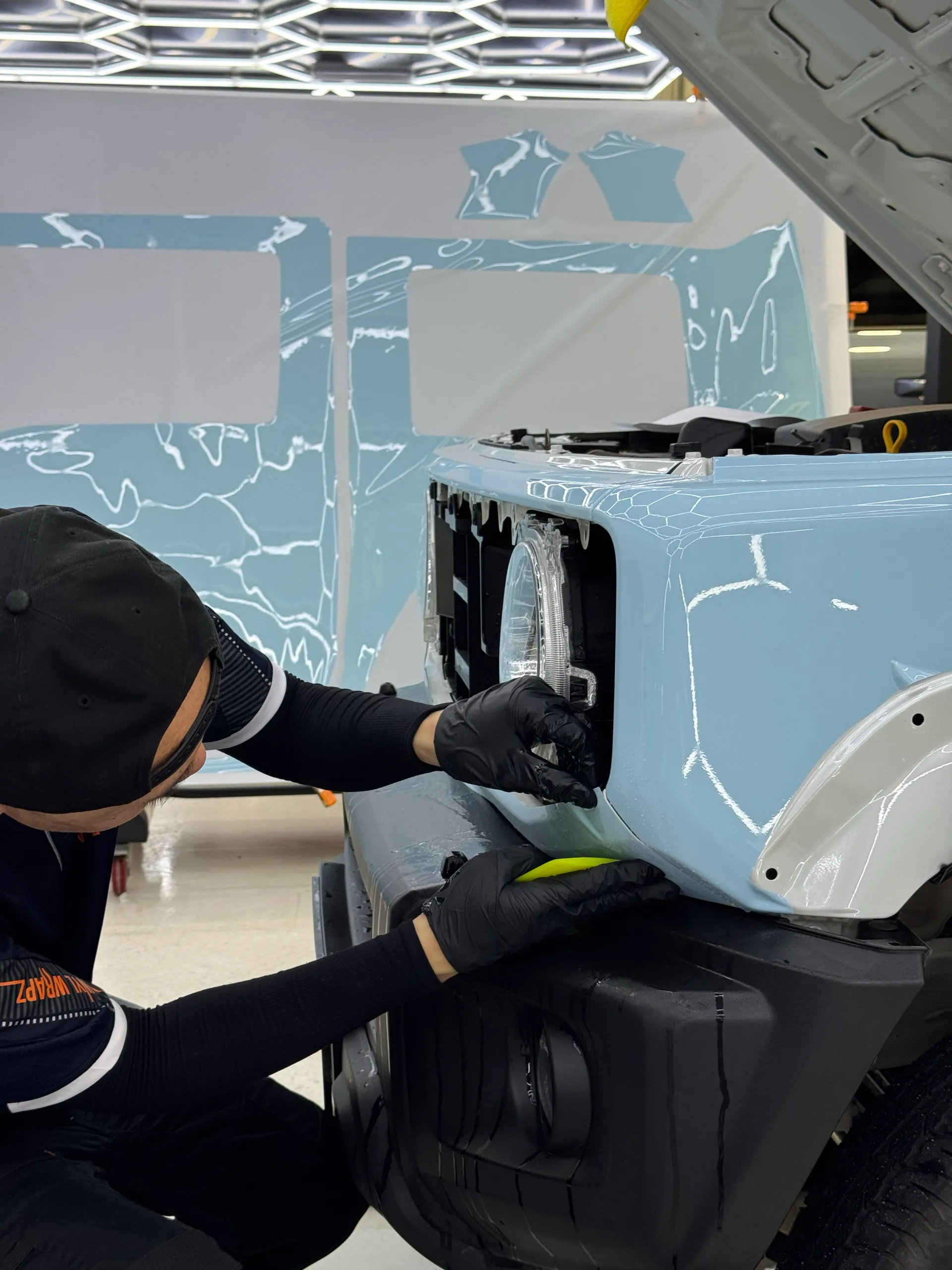 Installer fitting light blue film around the Suzuki Jimny headlight opening