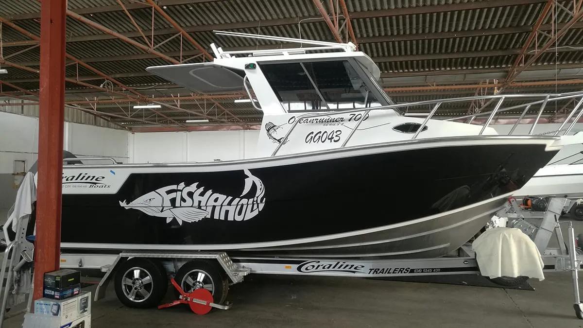 7 m Coraline Oceanrunner with a black gloss hull wrap and printed fish graphic on its trailer in the workshop
