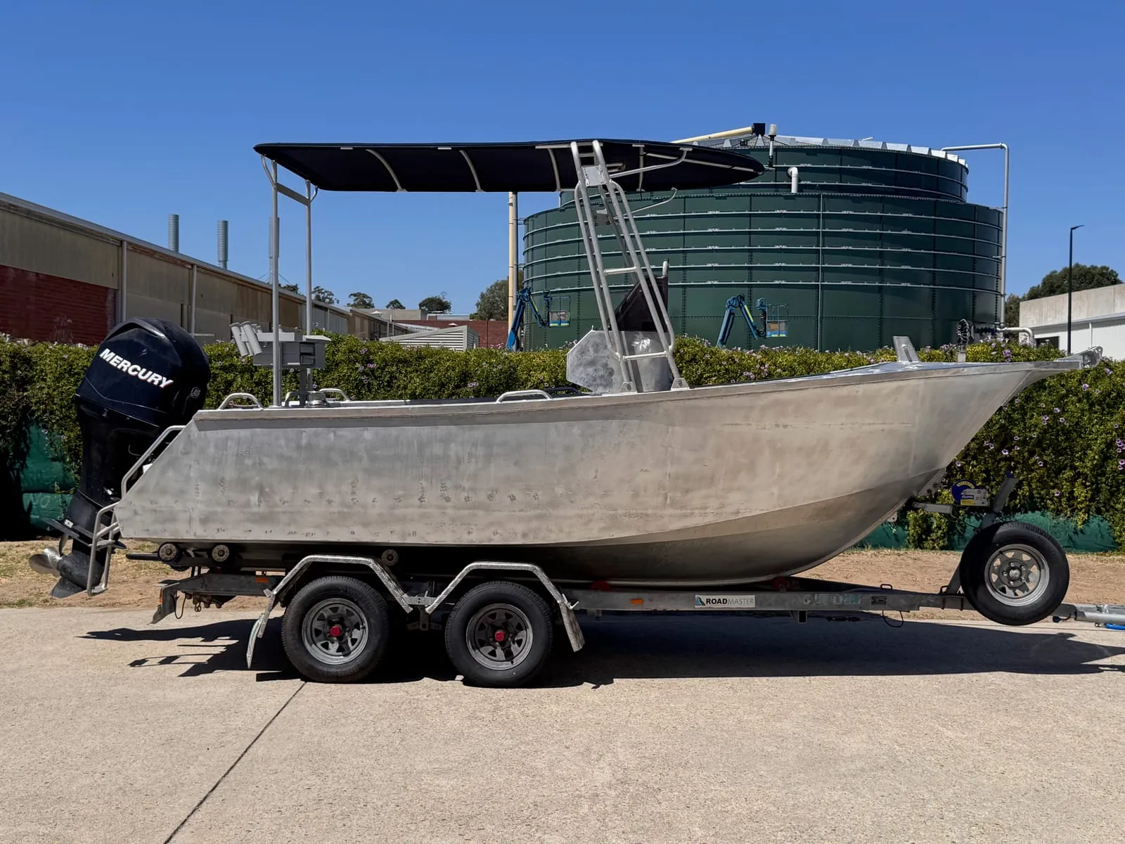 Bare aluminium centre-console fishing boat on its trailer outside the workshop, side on, before its wrap