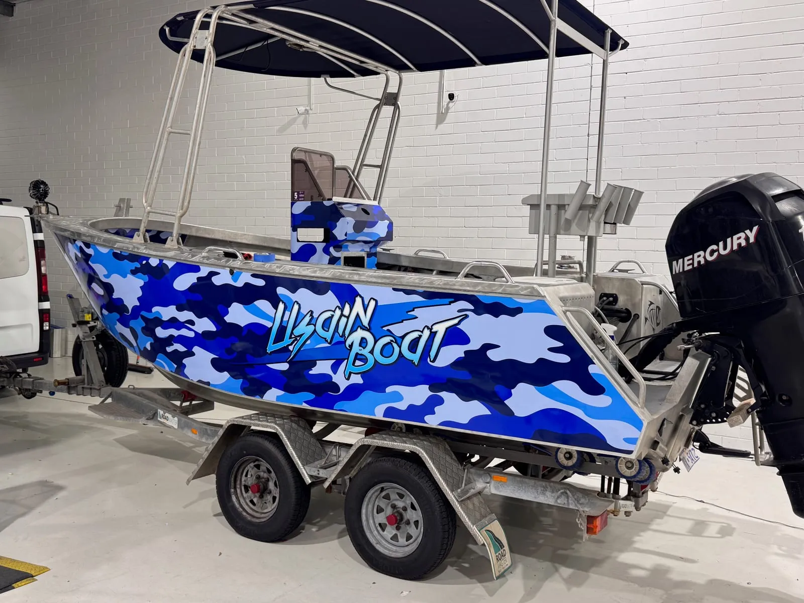Aluminium centre-console fishing boat in a custom printed blue camouflage hull wrap on its trailer in the Vinyl Wrapz workshop