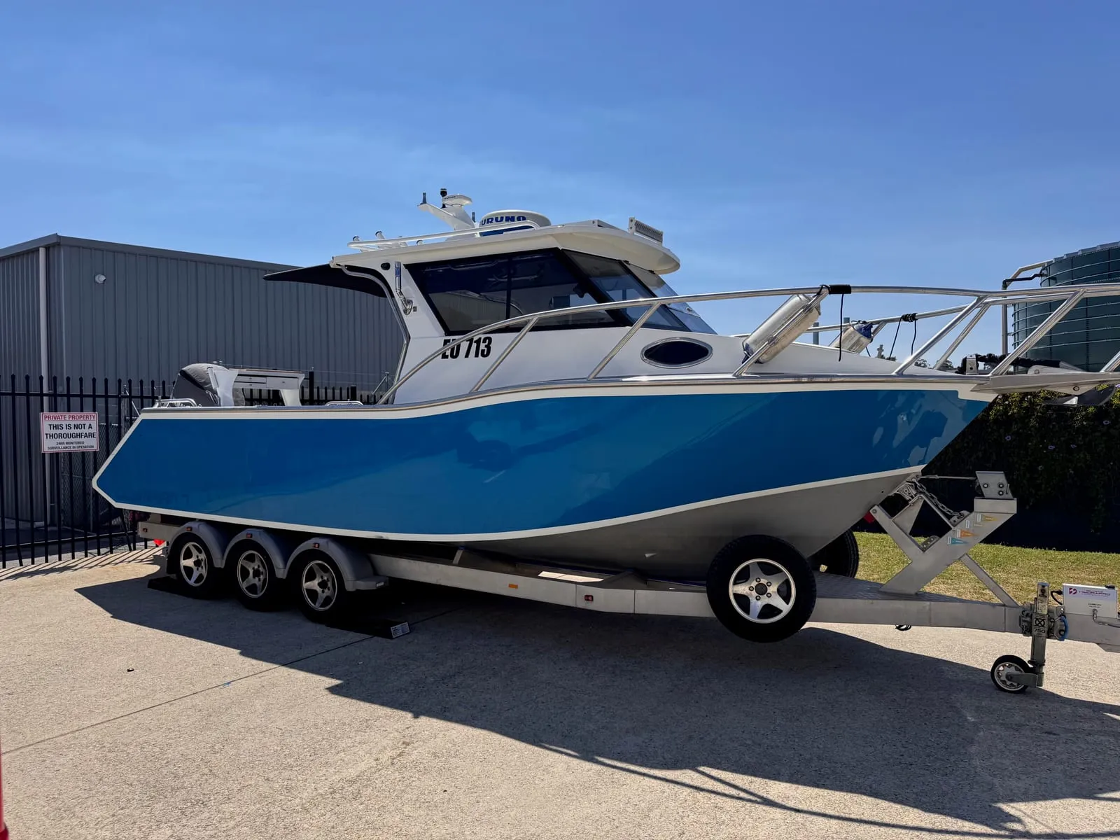 Gloss blue cabin cruiser on its triple-axle trailer outside the Vinyl Wrapz workshop, photographed before its hull wrap