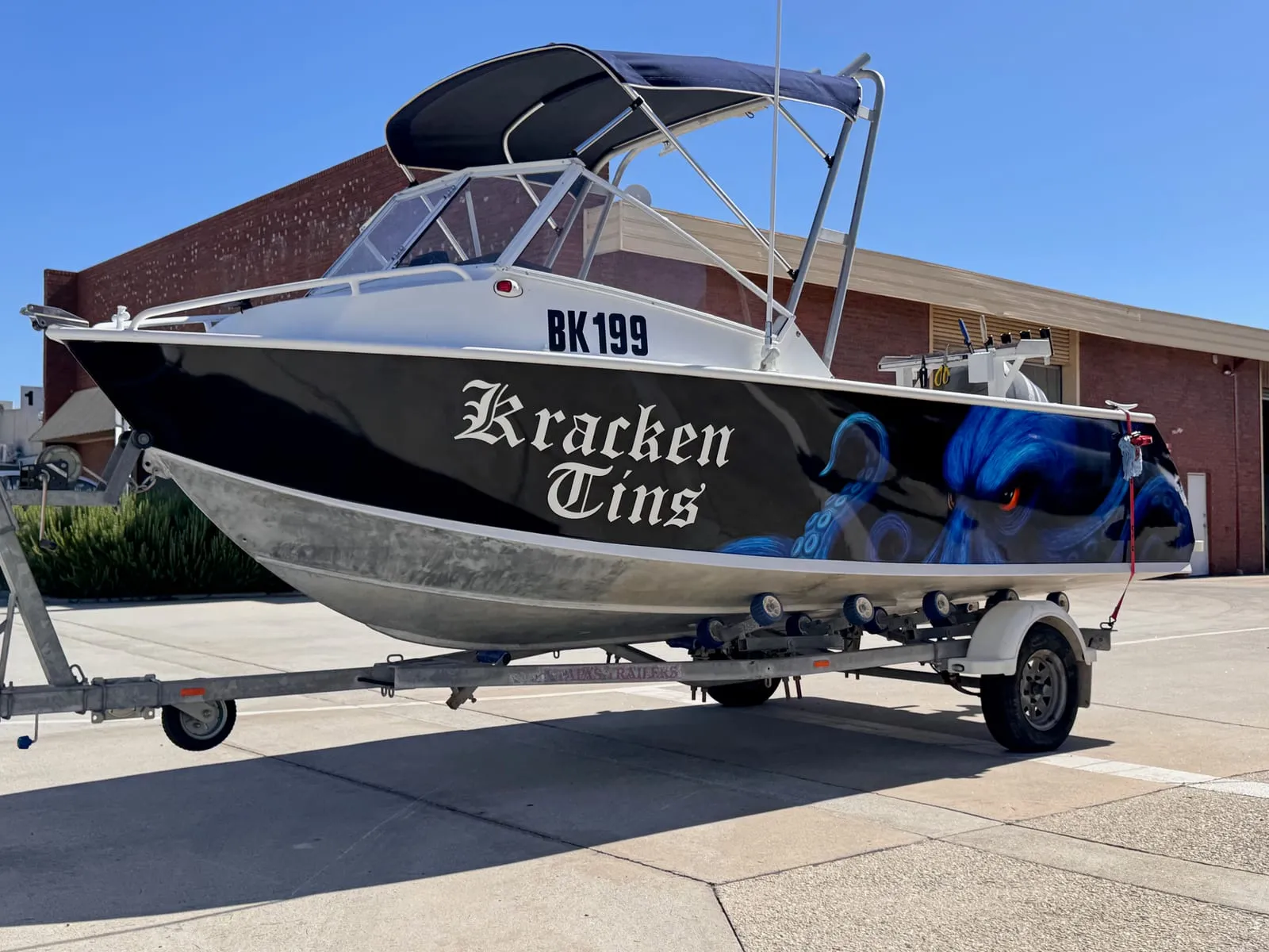 Kracken Tins aluminium boat with a printed blue octopus hull wrap, front three-quarter view outside the workshop