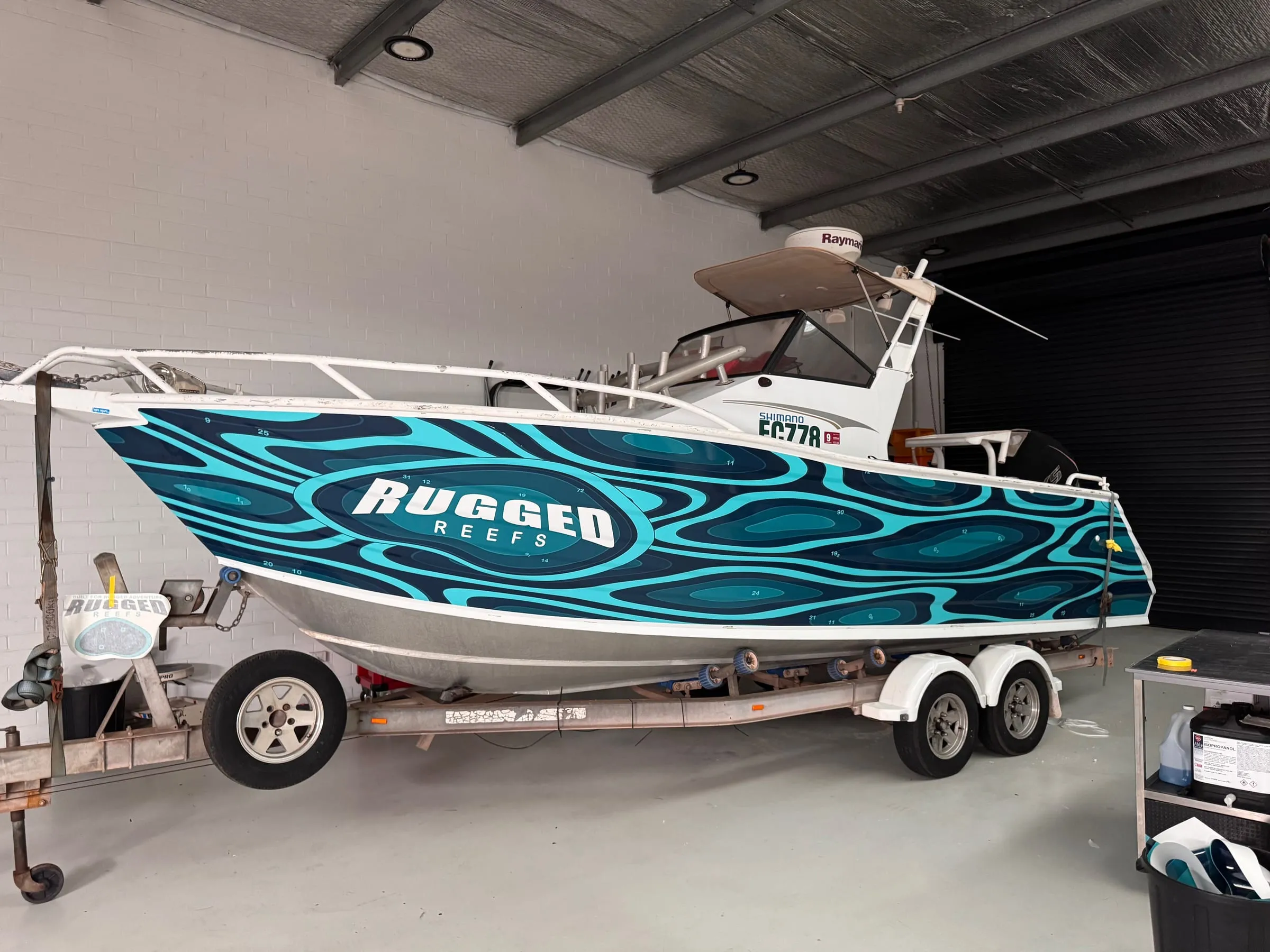 Centre-console fishing boat with a printed teal wave-pattern hull wrap in the workshop