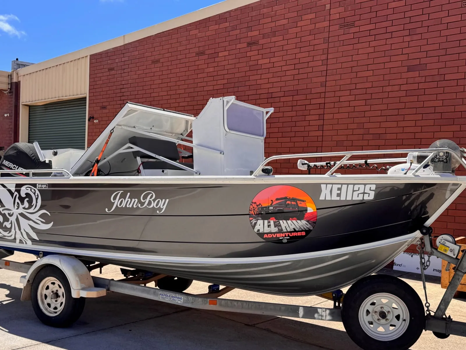 Satin dark grey aluminium boat hull wrap with printed business logo, boat name and registration lettering outside the workshop